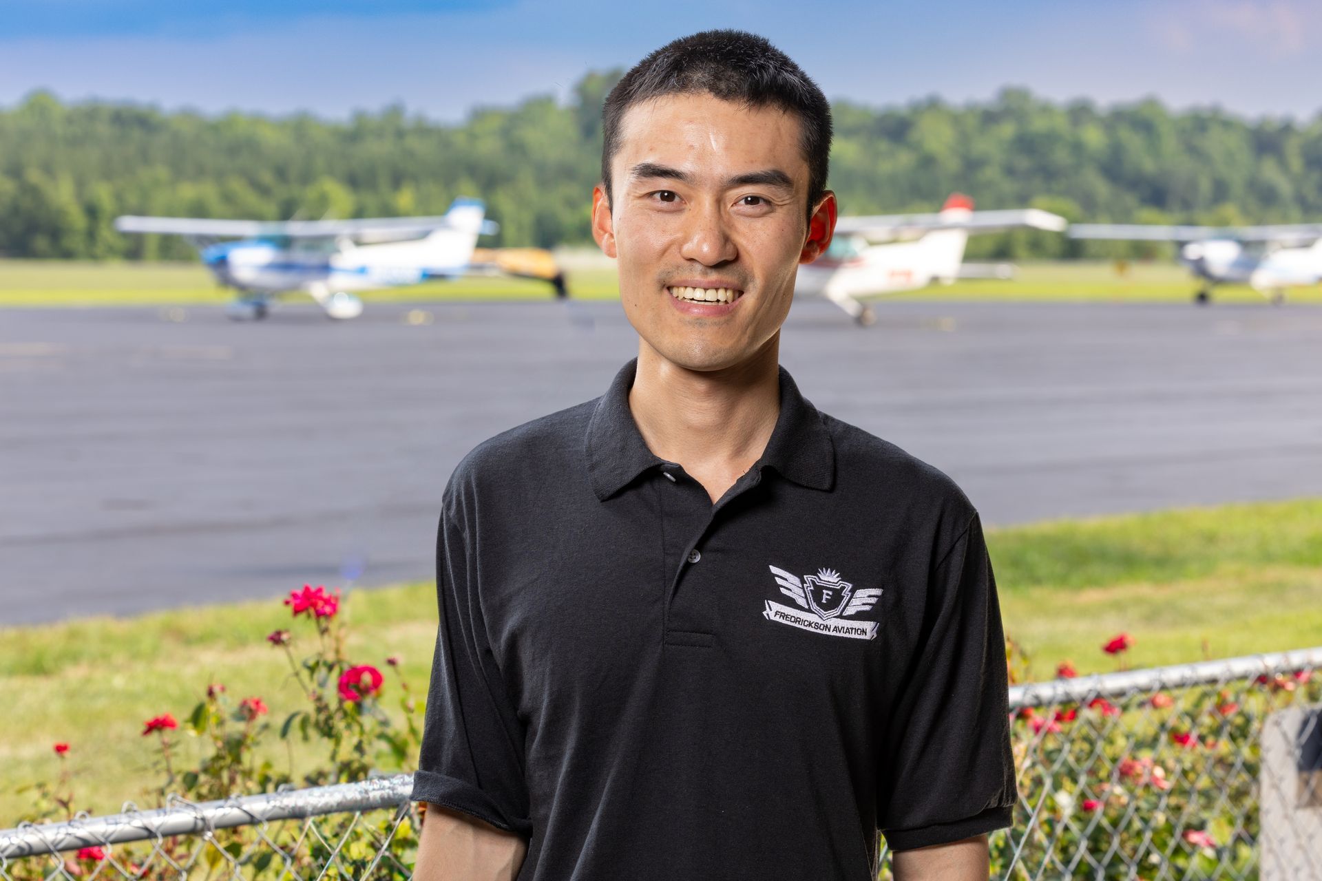 A man is standing in front of a runway with planes in the background.