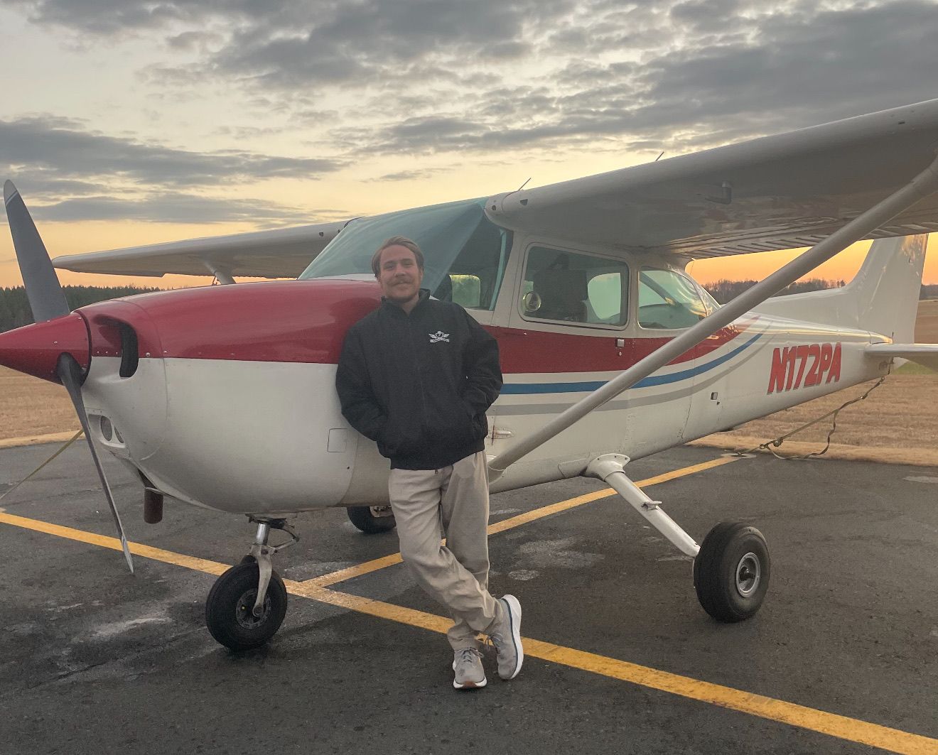 A man is standing in front of a runway with planes in the background.