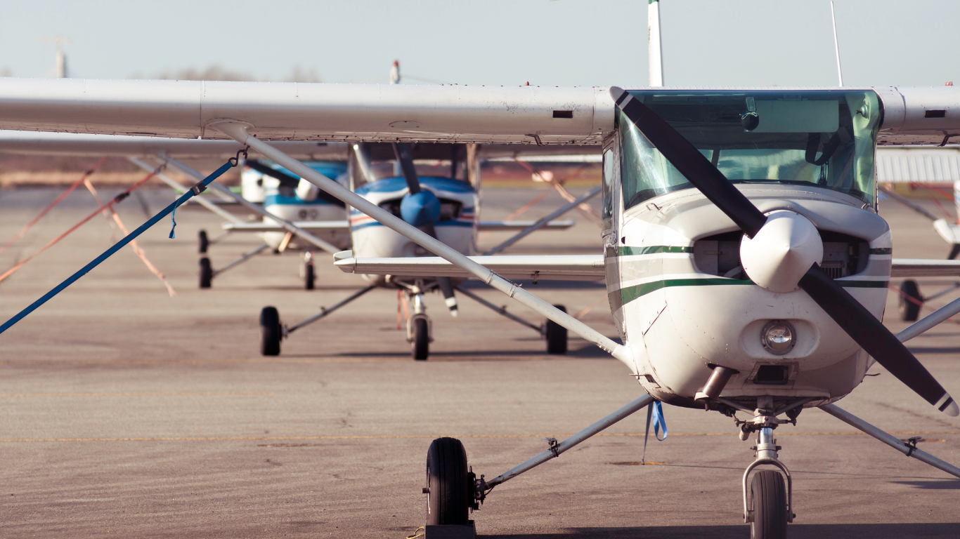 A row of small planes are parked on a runway