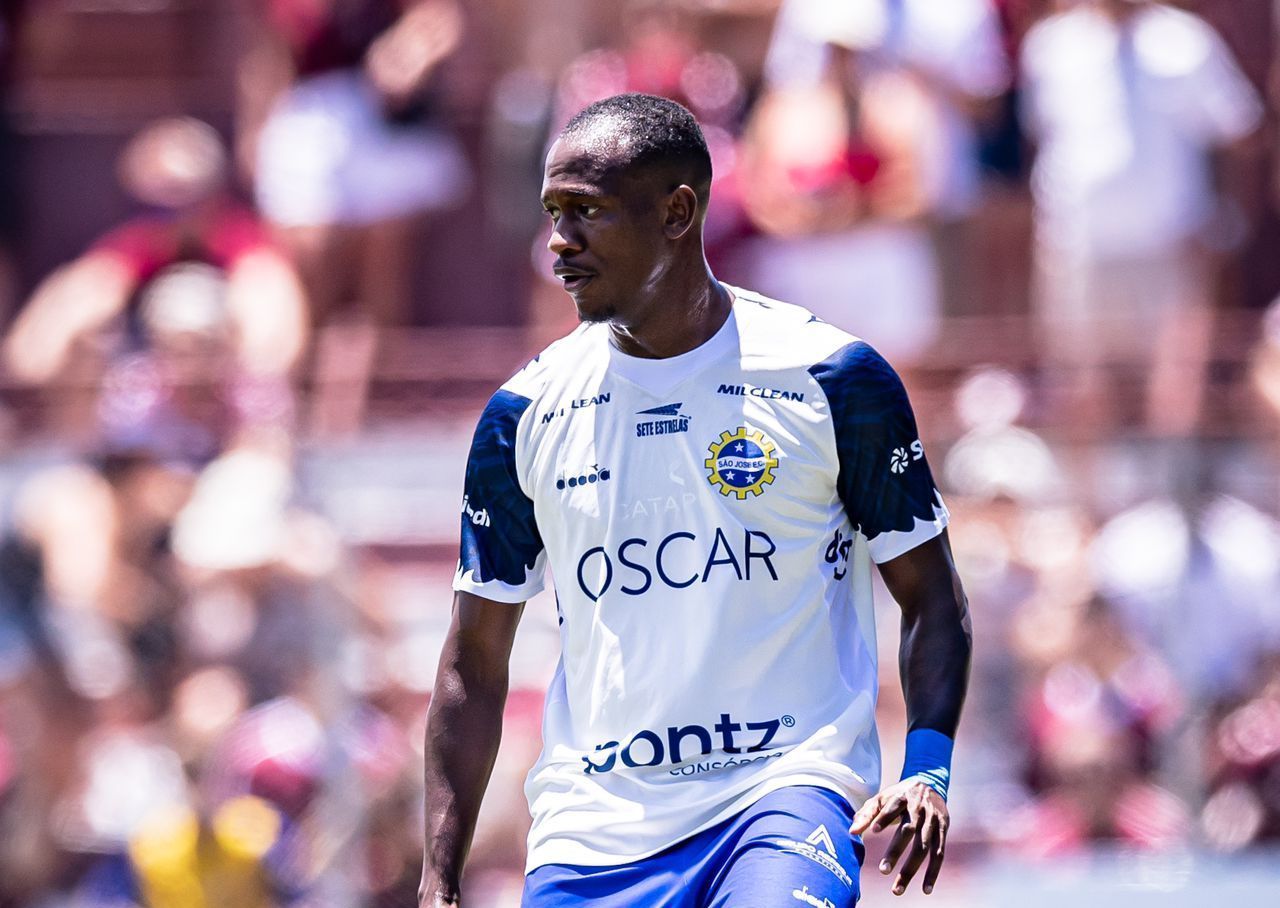 Um homem de camisa azul e shorts branco está jogando futebol