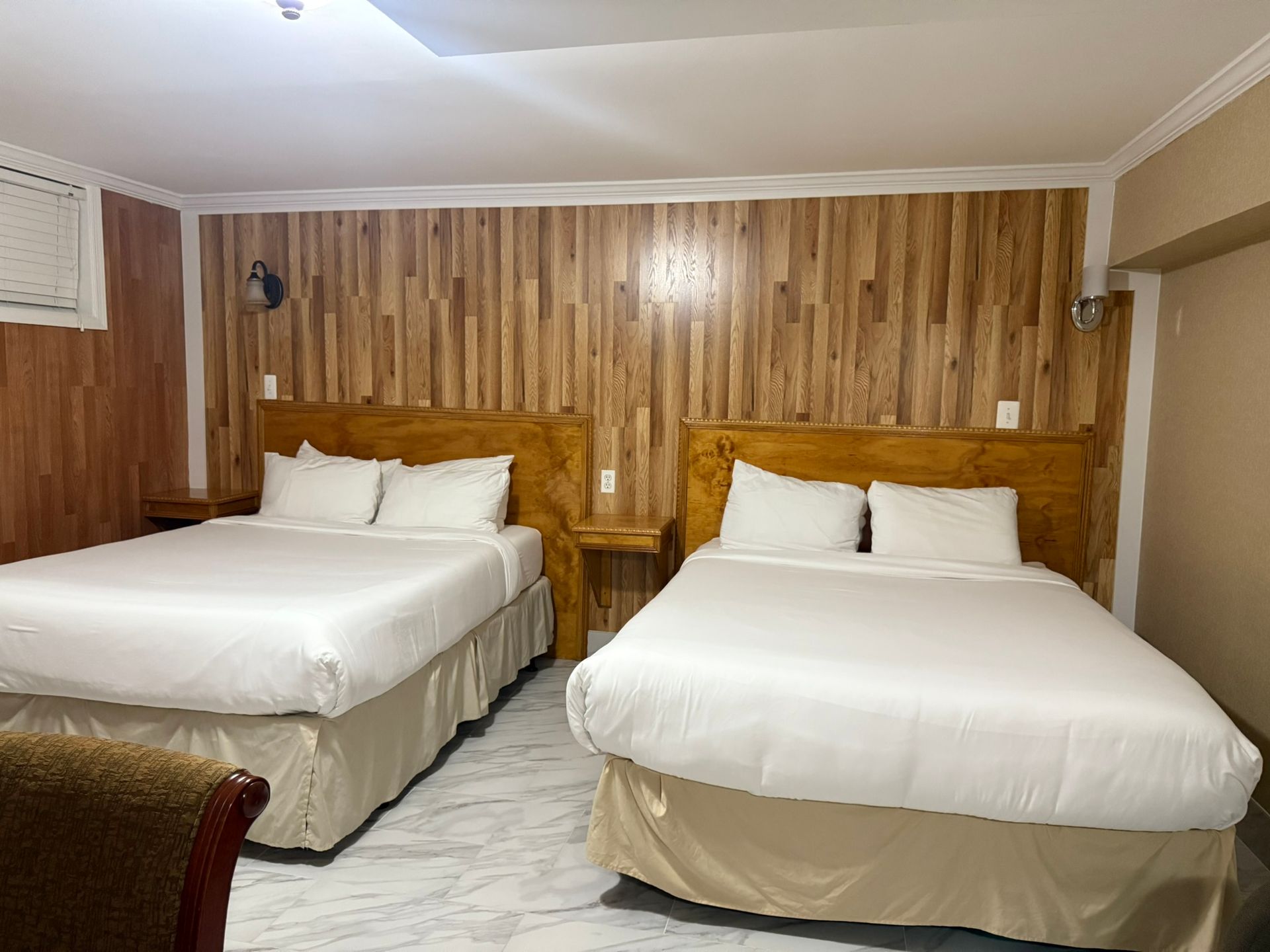 Two beds with white bedding in a room with wood paneling and a marble floor.