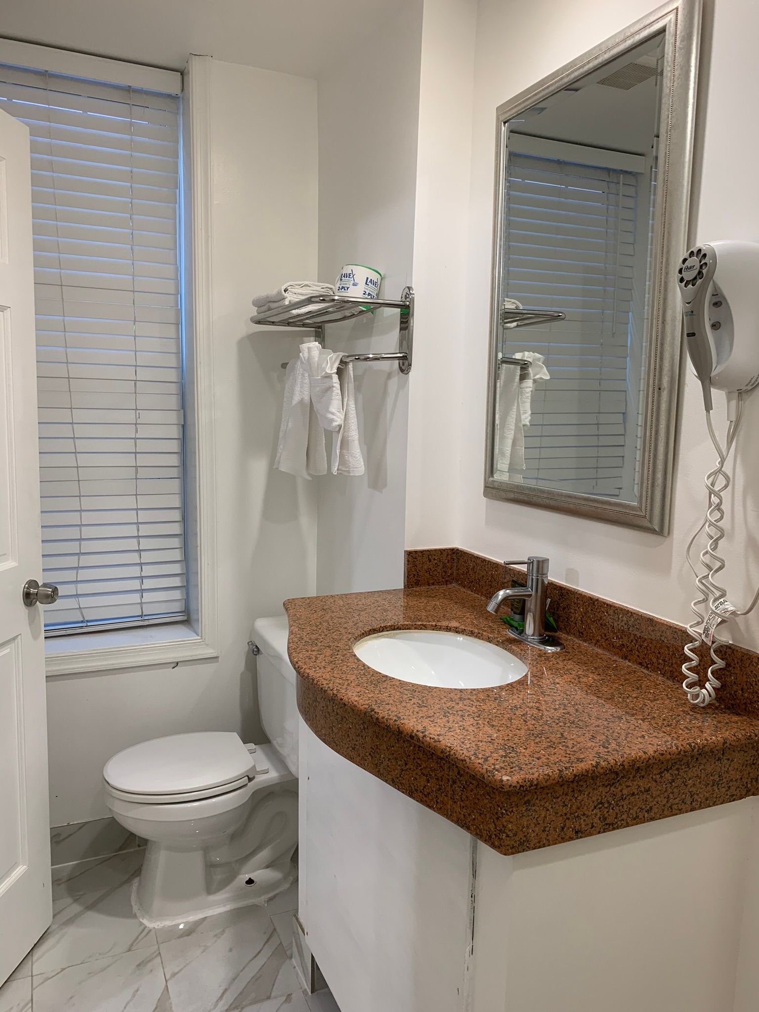 Small bathroom with a toilet, sink, and shower area. The sink has a granite countertop and a mirror.