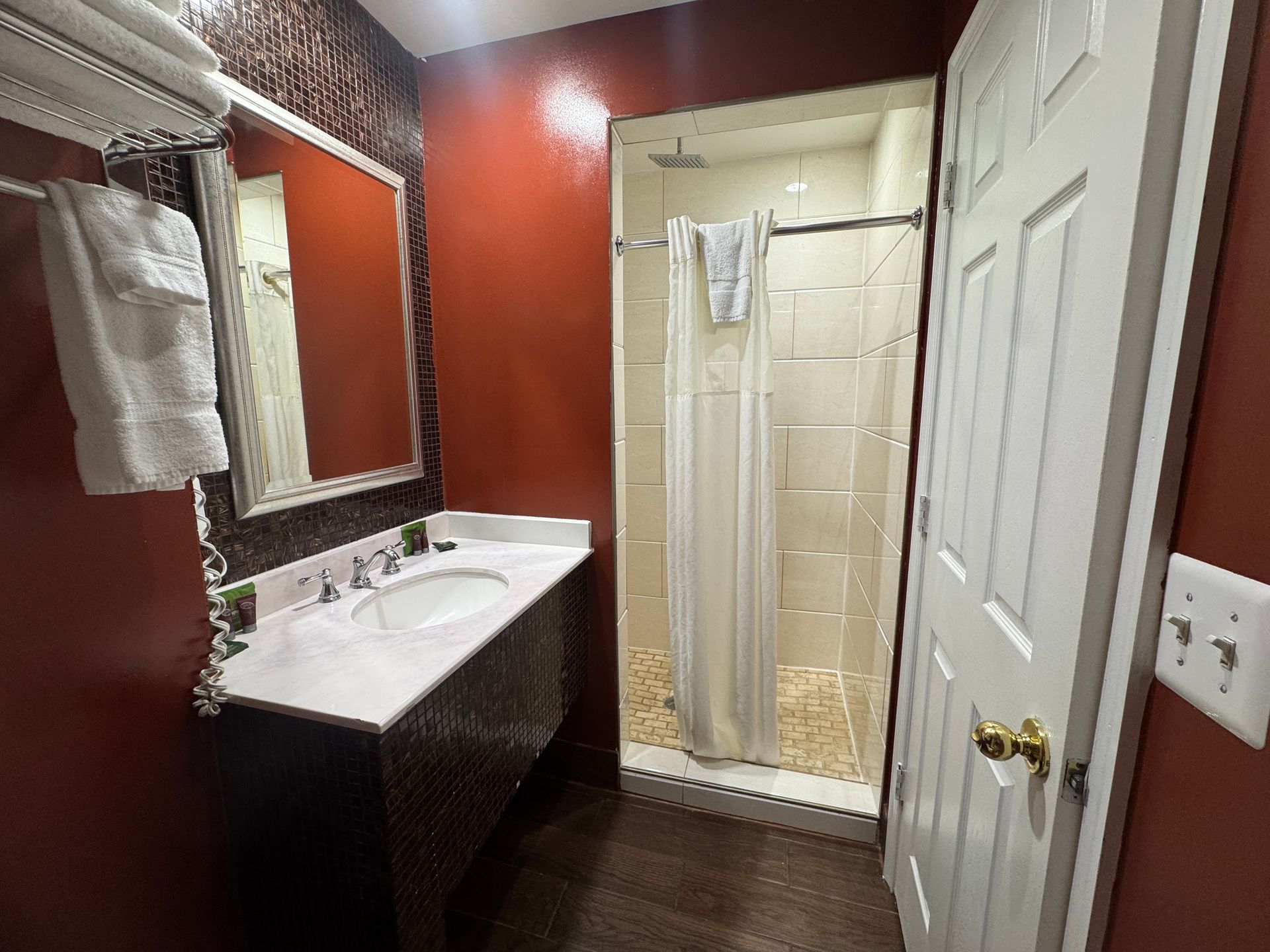 Bathroom with red walls, a shower, sink, mirror, and white door.