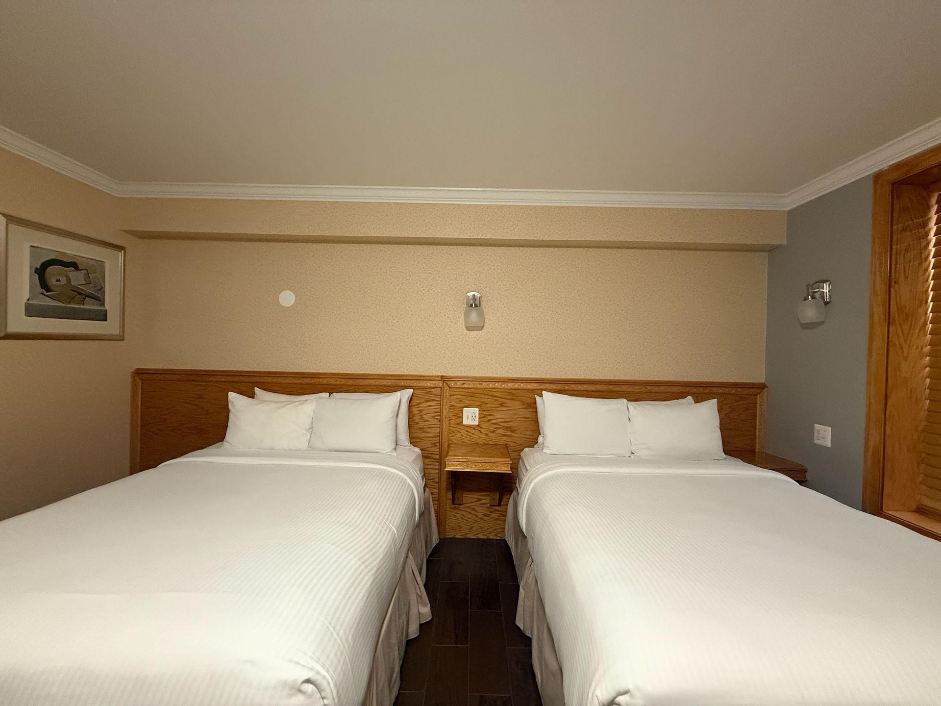 A hotel room with two twin beds covered in white bedding. A small nightstand sits between the beds.