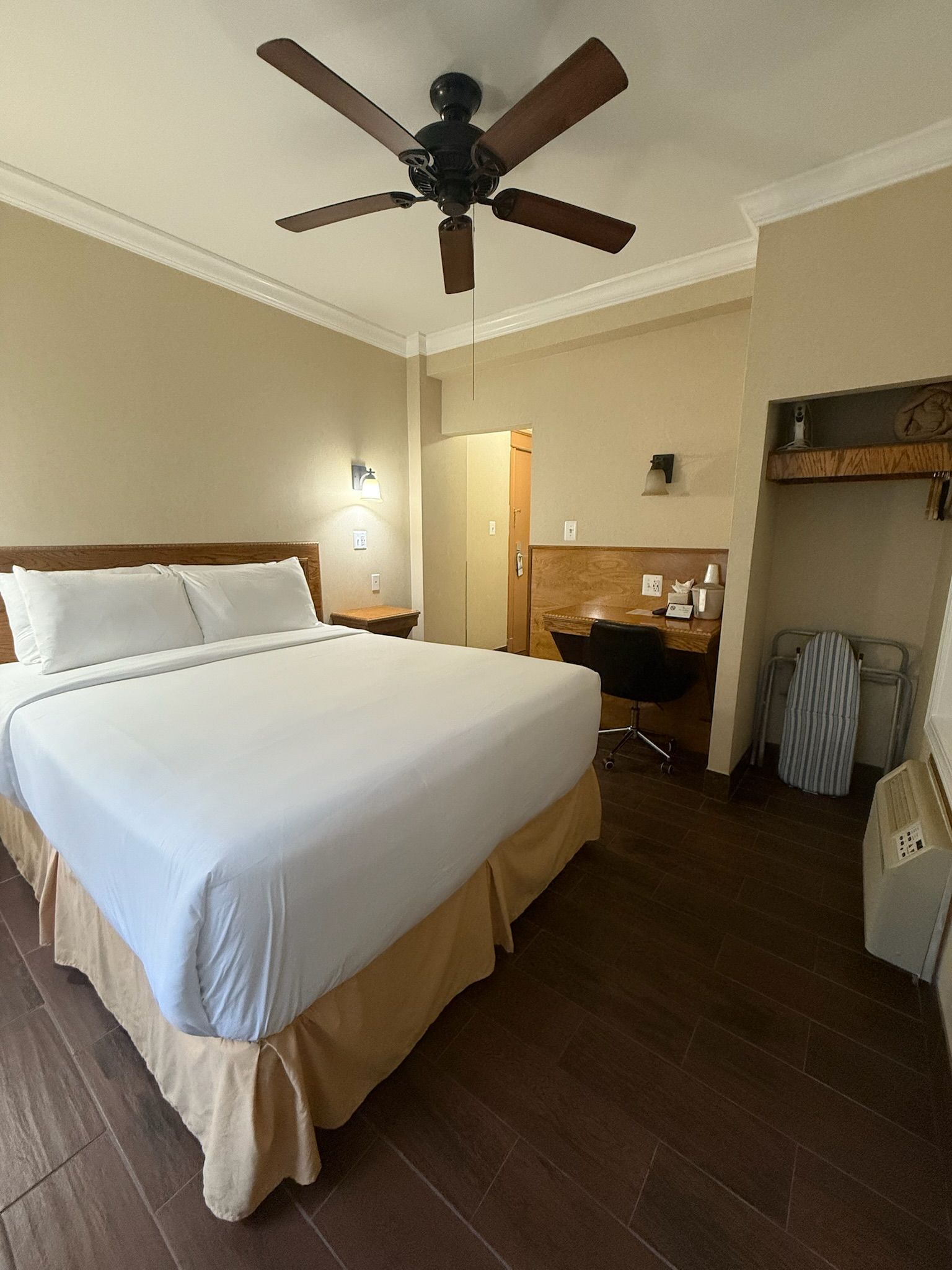 Bedroom with a king-sized bed, desk, closet, and ceiling fan. Light tan walls, dark brown hardwood floors.