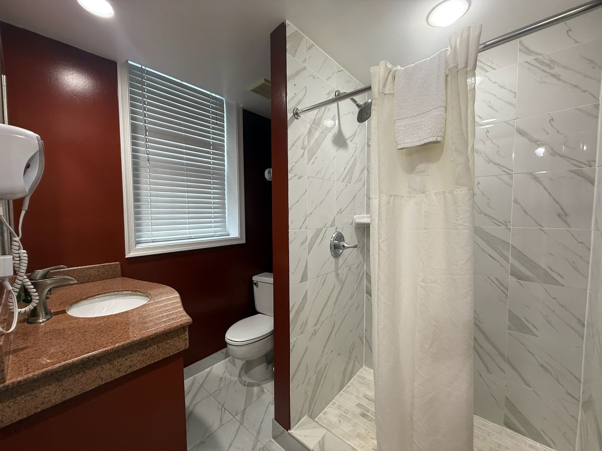 Bathroom with red walls, white marble tile, shower with curtain, toilet, and sink.