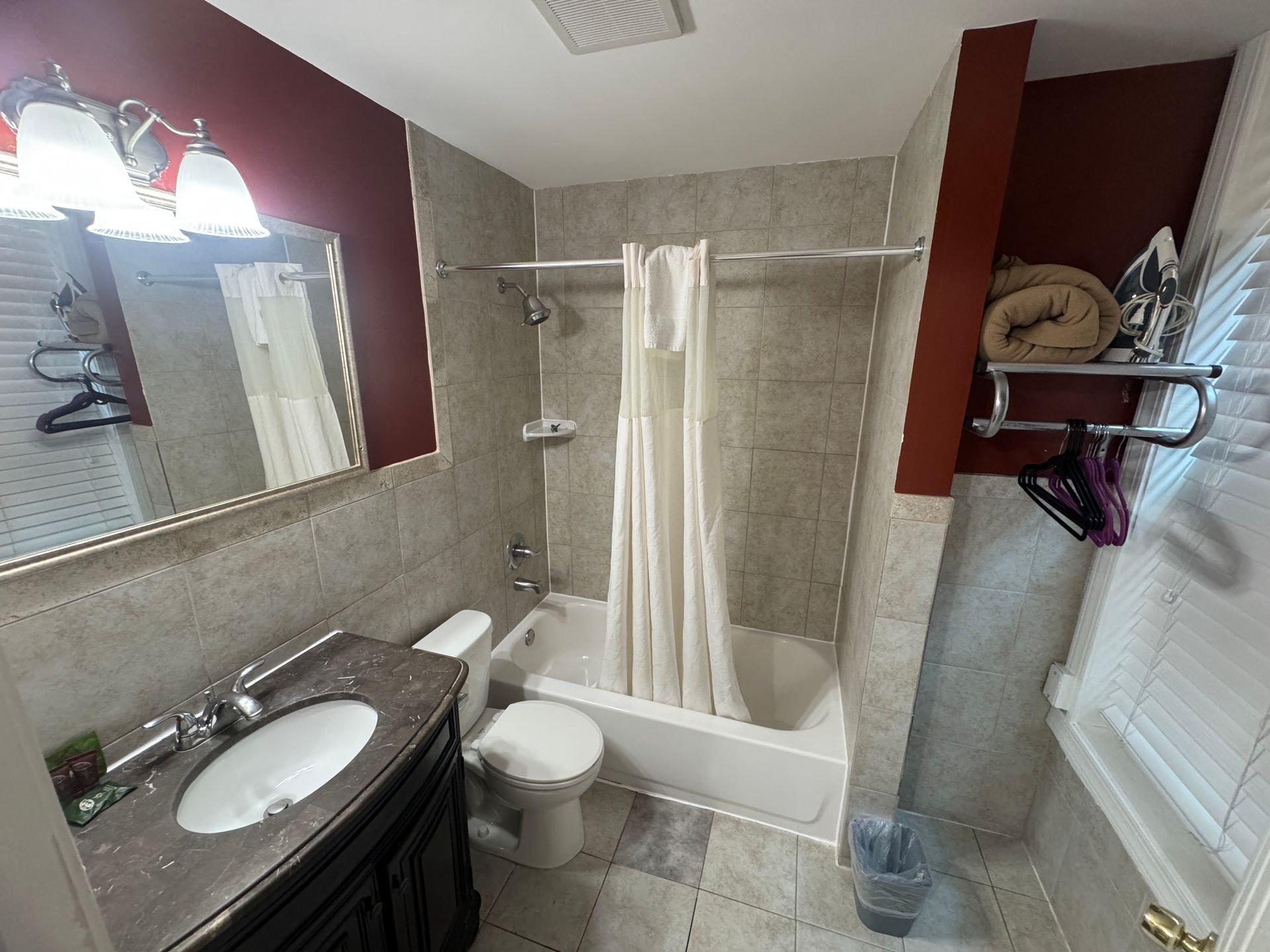 Bathroom with a vanity, toilet, bathtub, and shower curtain. Walls are gray and dark red; a towel rack and window.