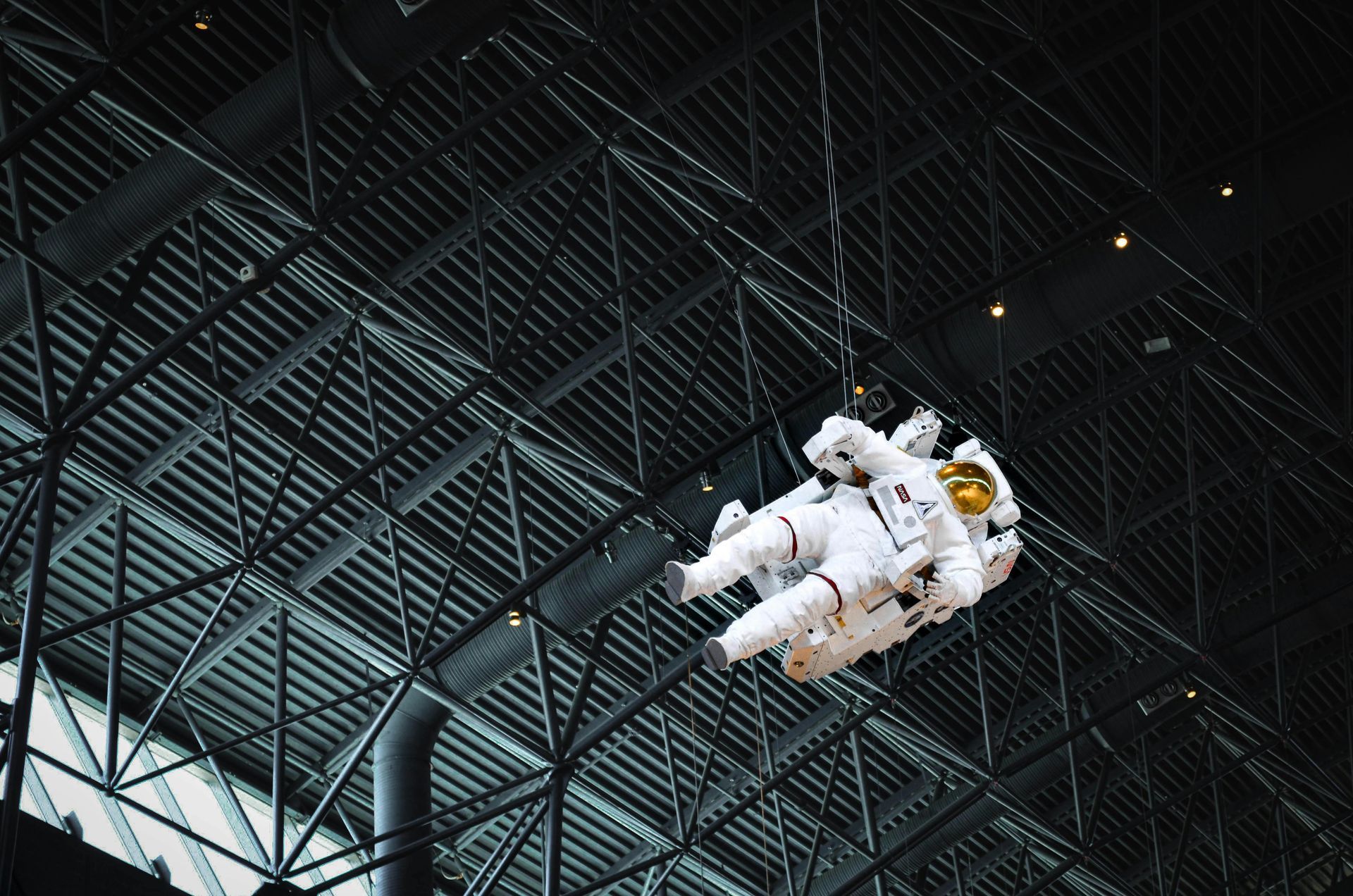 A statue of an astronaut is hanging from the ceiling of a building.