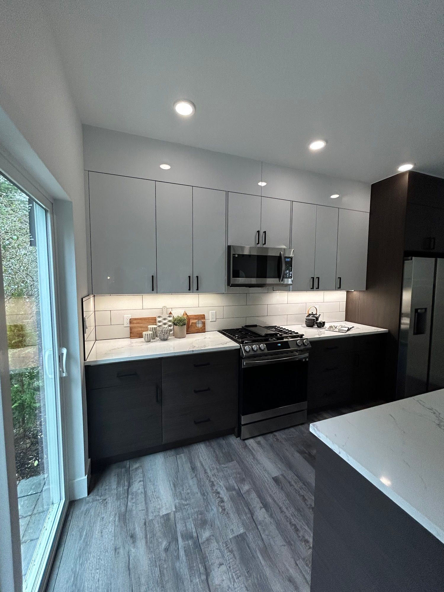 Modern kitchen with gray and dark cabinets, stainless steel appliances, and white countertops.