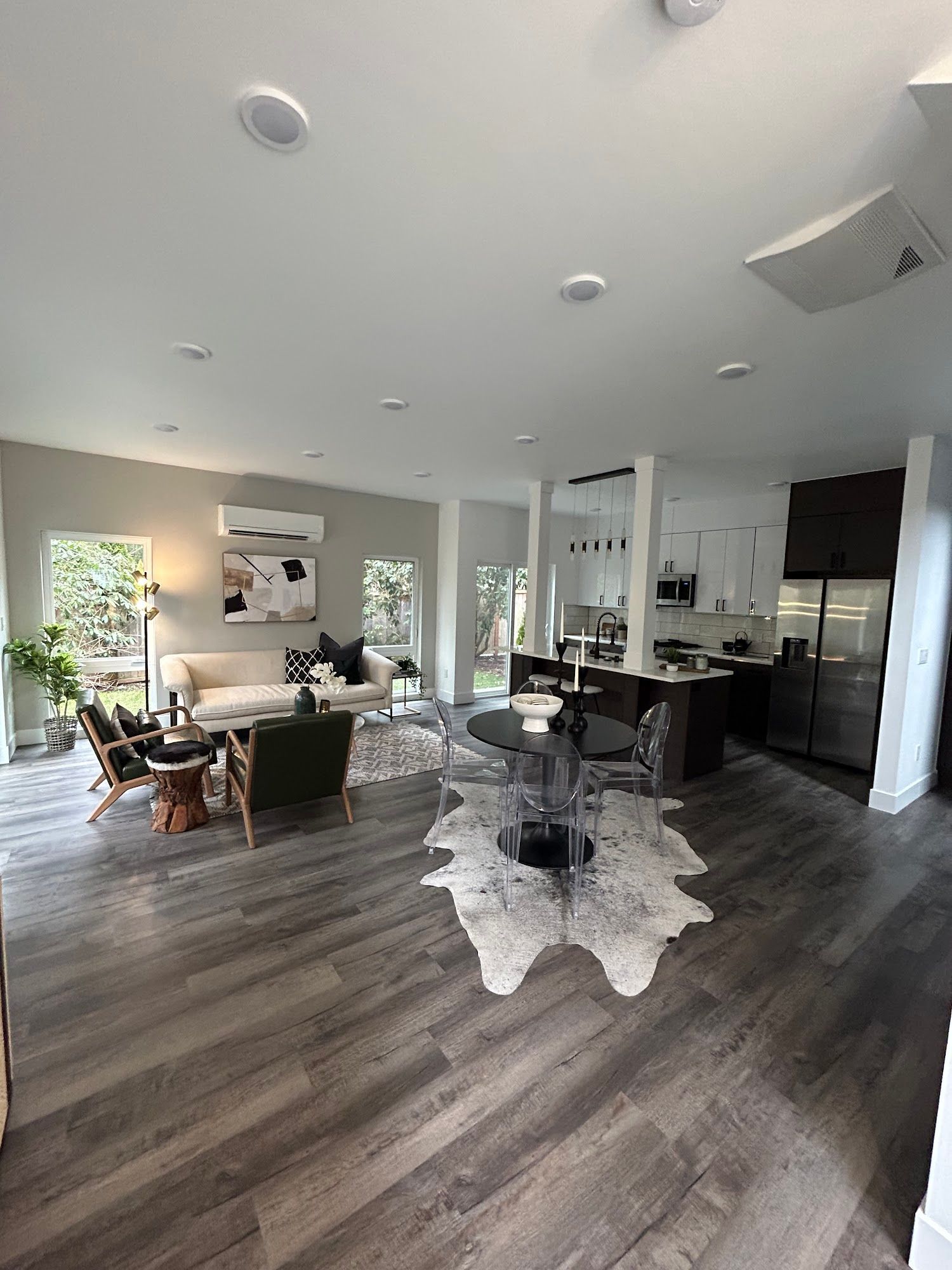 Open-concept living space with gray wood floors, kitchen, living room with seating, and a decorative rug.