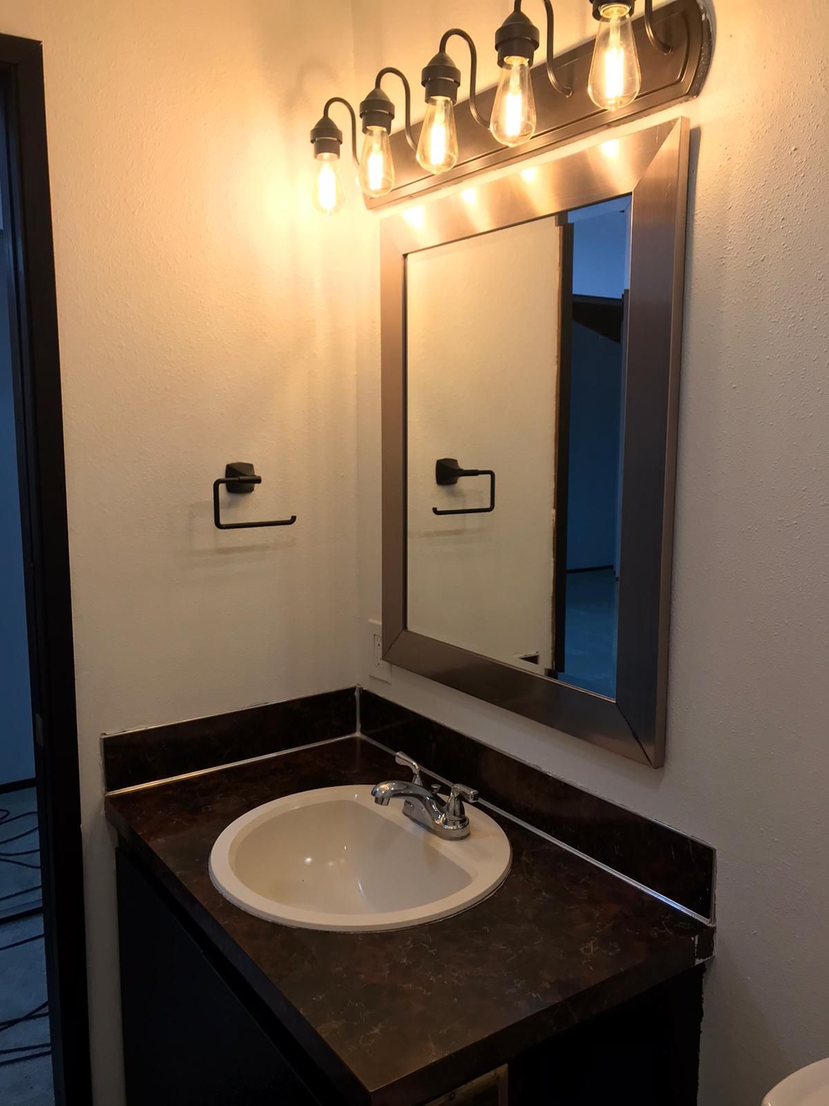 Bathroom with a mirror, sink, and light fixture. Black vanity, brown countertop, and white walls.