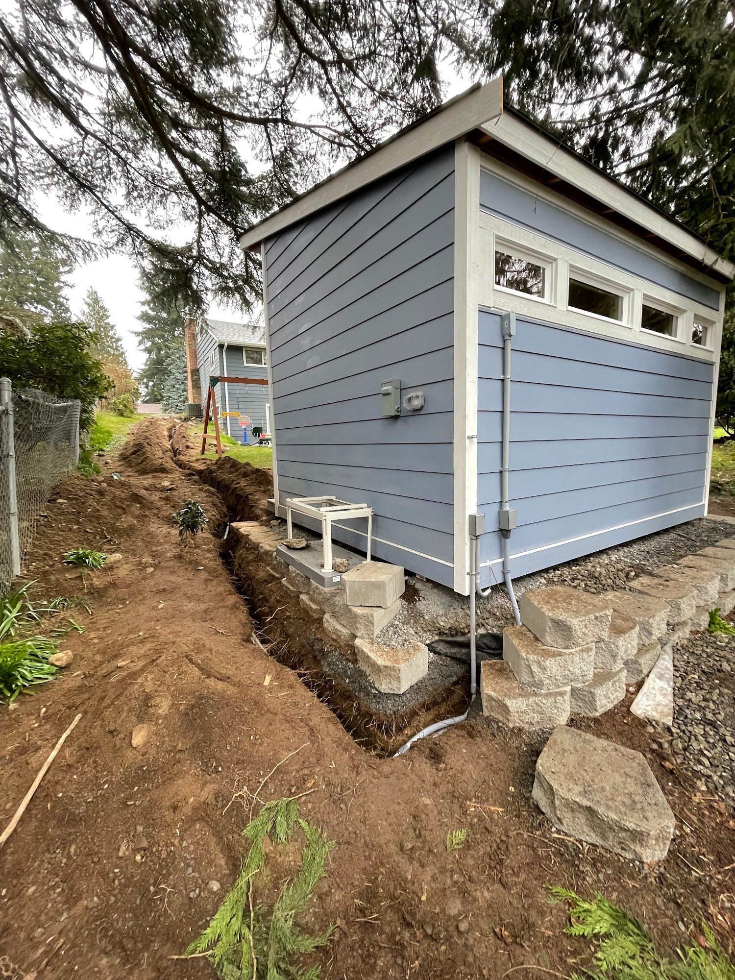 A light blue shed being built next to a dirt trench on a hill.