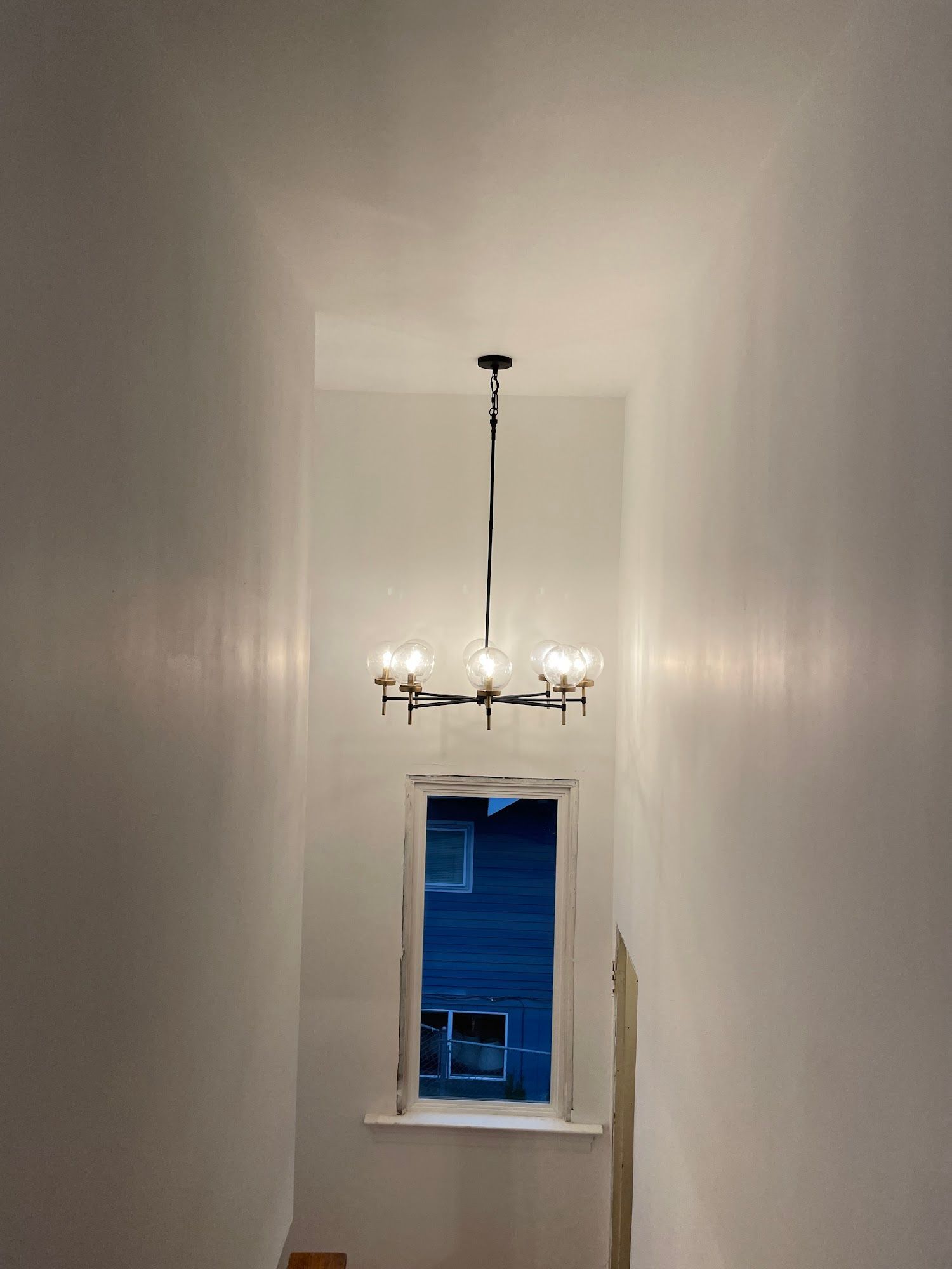 Narrow hallway with white walls, chandelier, and a window covered in blue plastic.