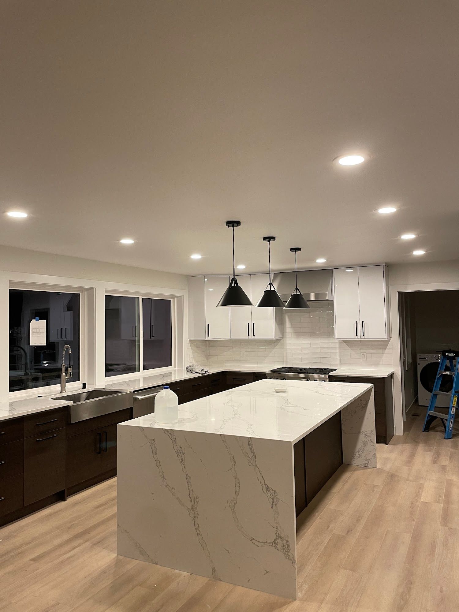 Modern kitchen with island, pendant lights, two-toned cabinets, light countertops, and recessed ceiling lights.