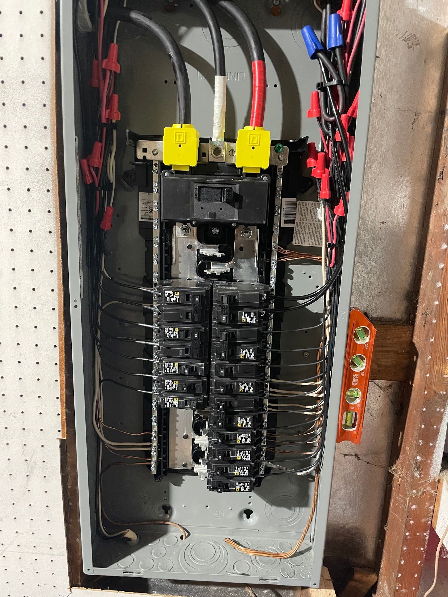 Electrical panel with numerous wires and circuit breakers, installed inside a wall.
