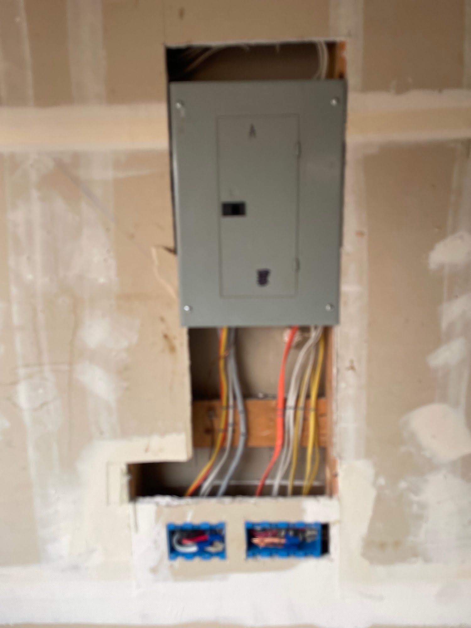 Electrical panel installed in a wall. Wires and electrical boxes visible below.