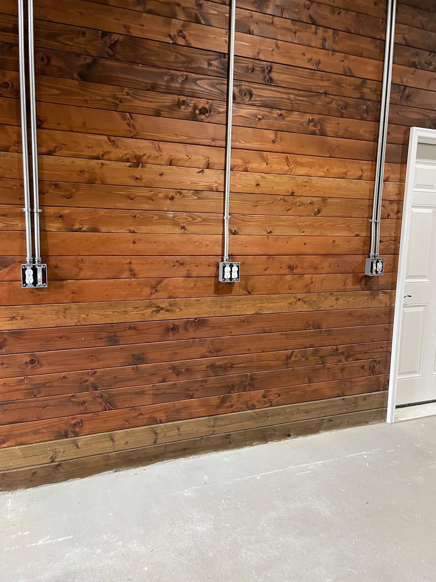 Wooden wall with three silver conduit pipes and electrical boxes. A white door is on the right.