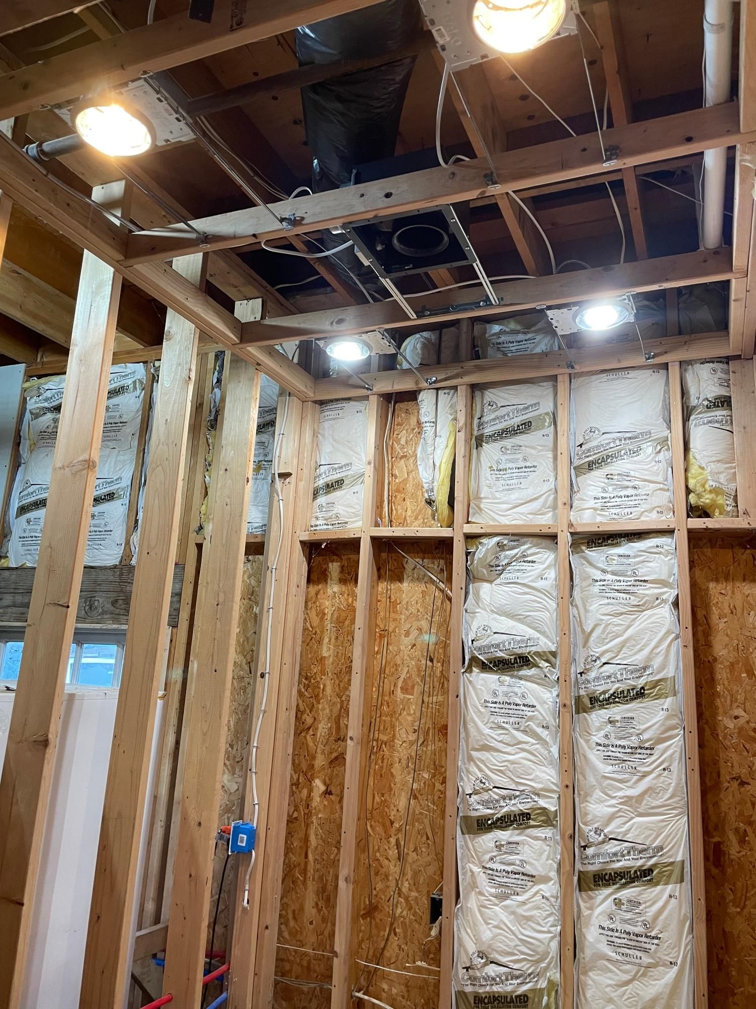 Interior view of a construction site with exposed wooden framing, insulation, and electrical wiring for a room.
