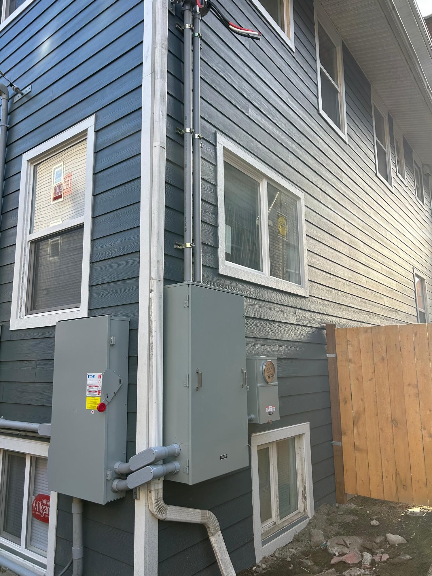 Exterior of a building with blue siding and electrical equipment installed on the wall.