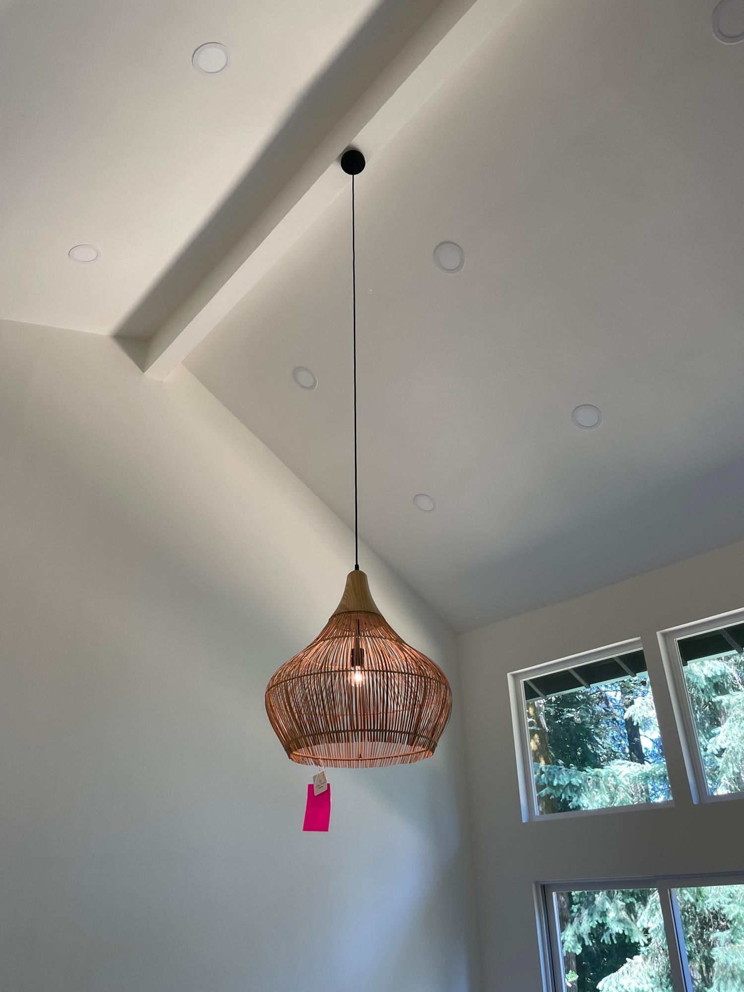 Woven pendant light fixture suspended from a white ceiling in a room with a window.