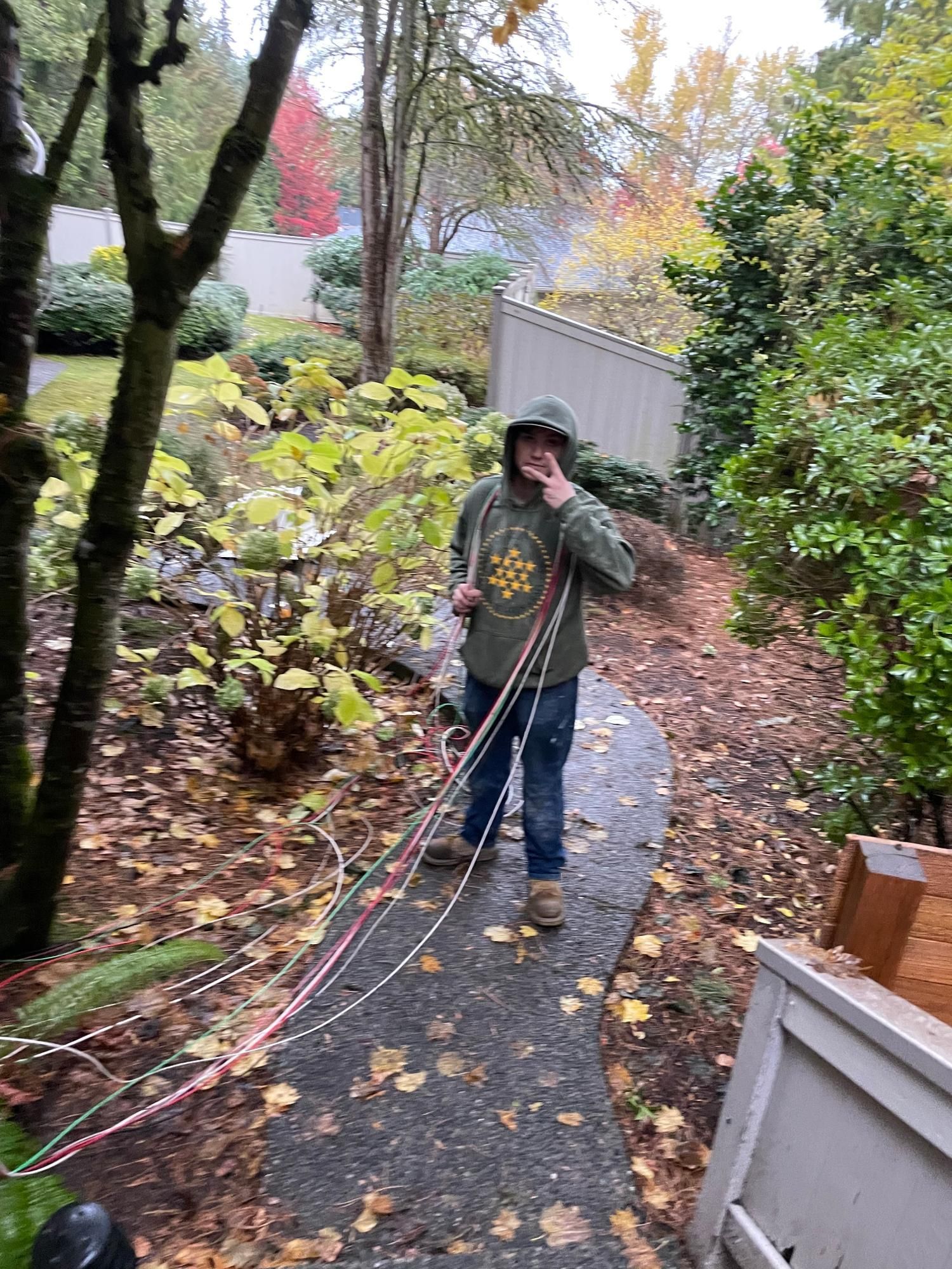 Person on a walkway holding wires, possibly working on landscaping. Fall foliage in the background.