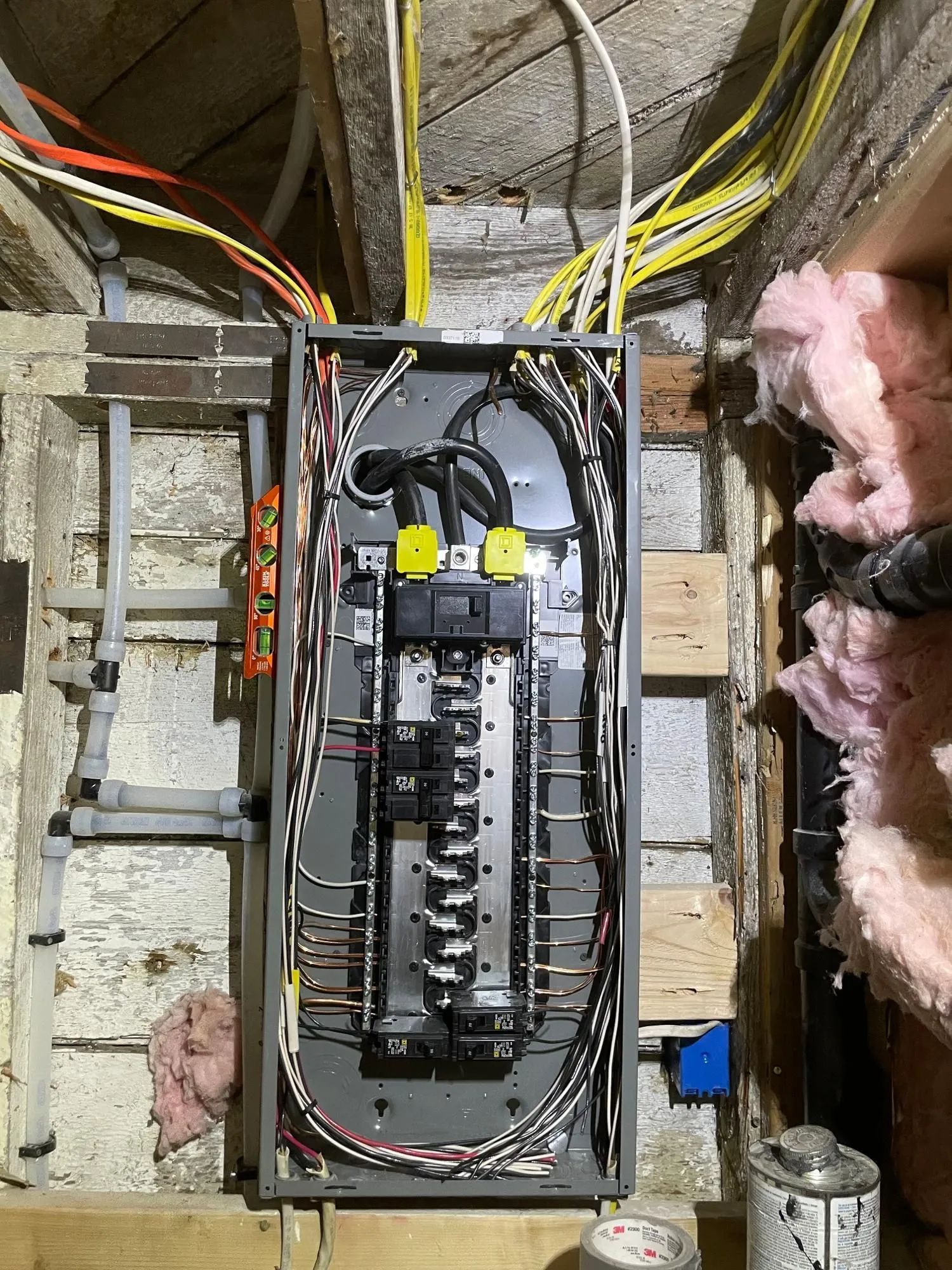 An open residential electrical breaker panel mounted on a wooden frame with various colored wiring connected to it.