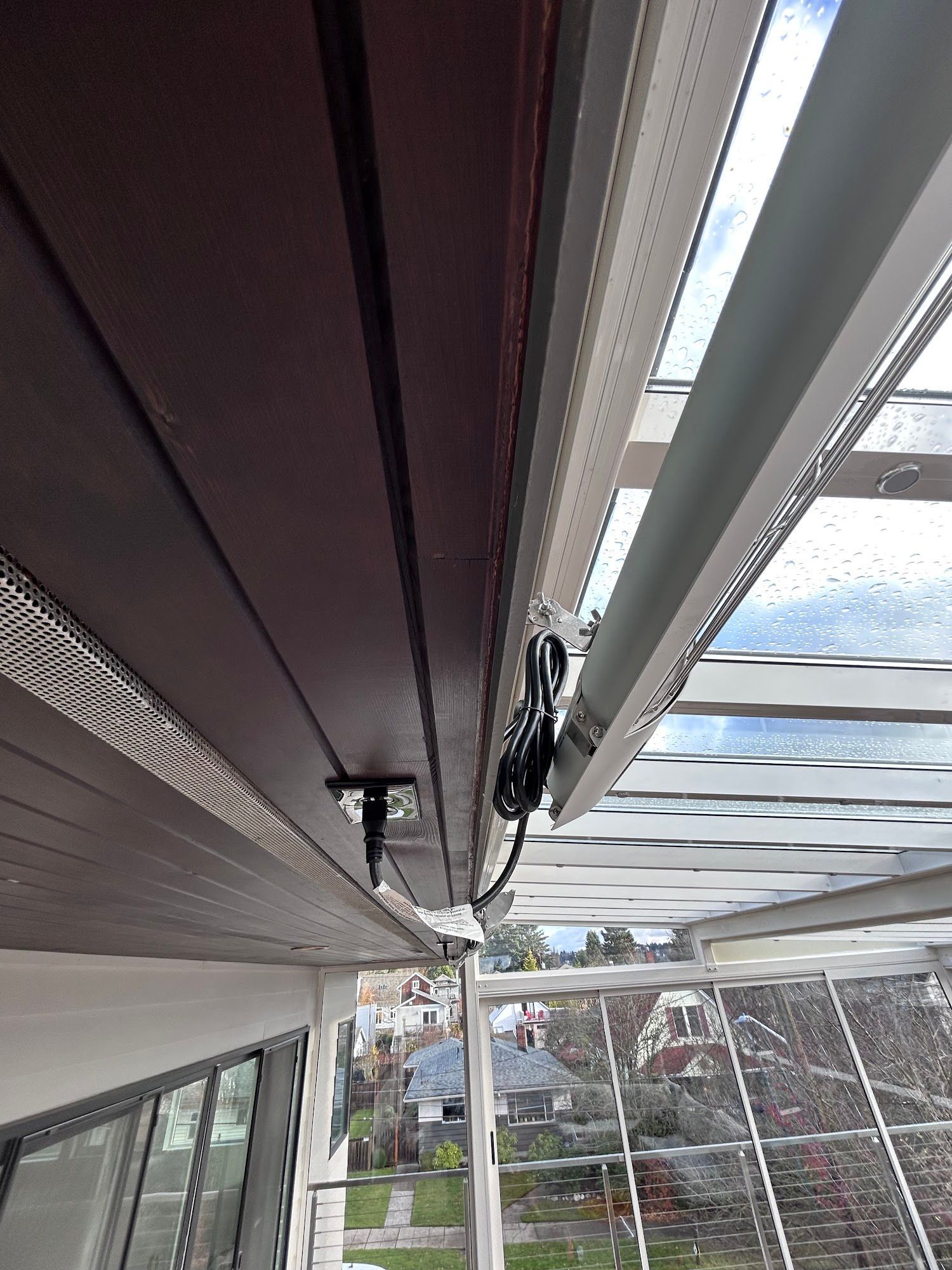 Overhead view of a ceiling with dark wood panels and a white track system, possibly for an awning or shade.