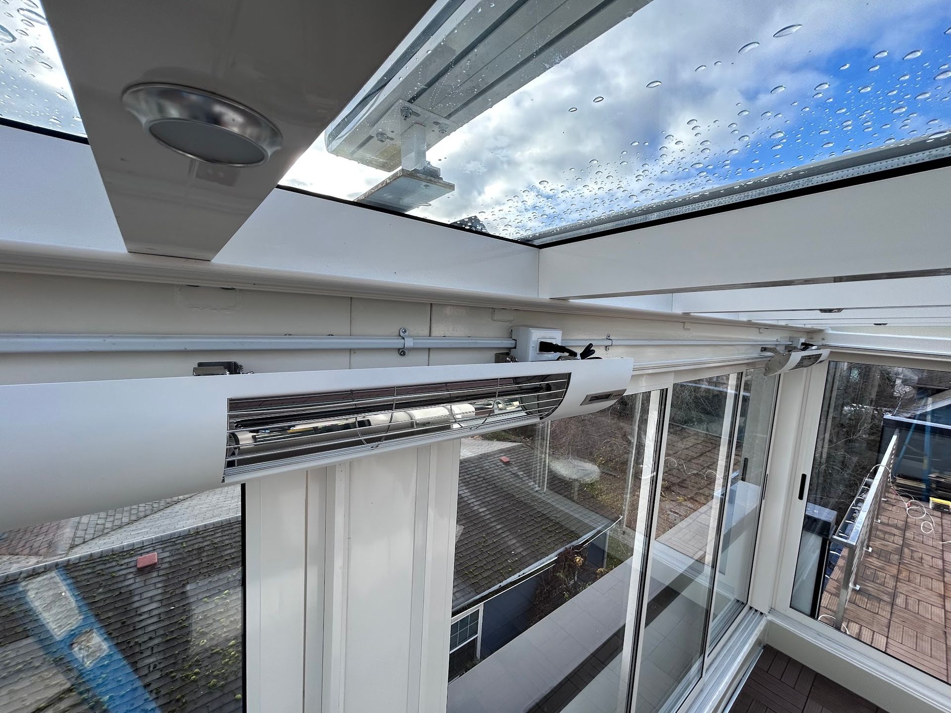 White infrared patio heater mounted on a glass-walled structure overlooking a city view.