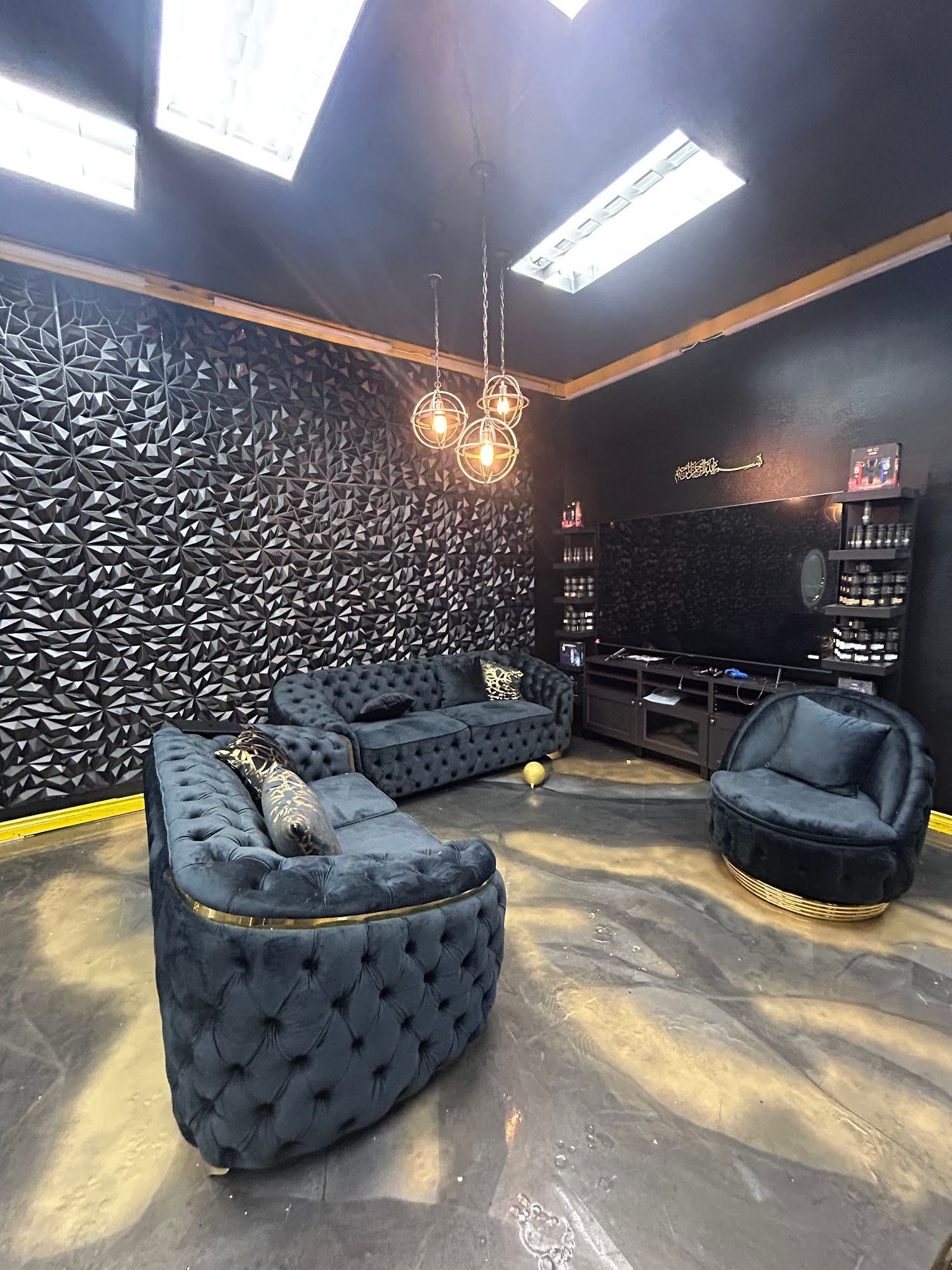 Dark-themed living room with black tufted sofa, chairs, and textured accent wall. Overhead lights, black ceiling, gold trim.