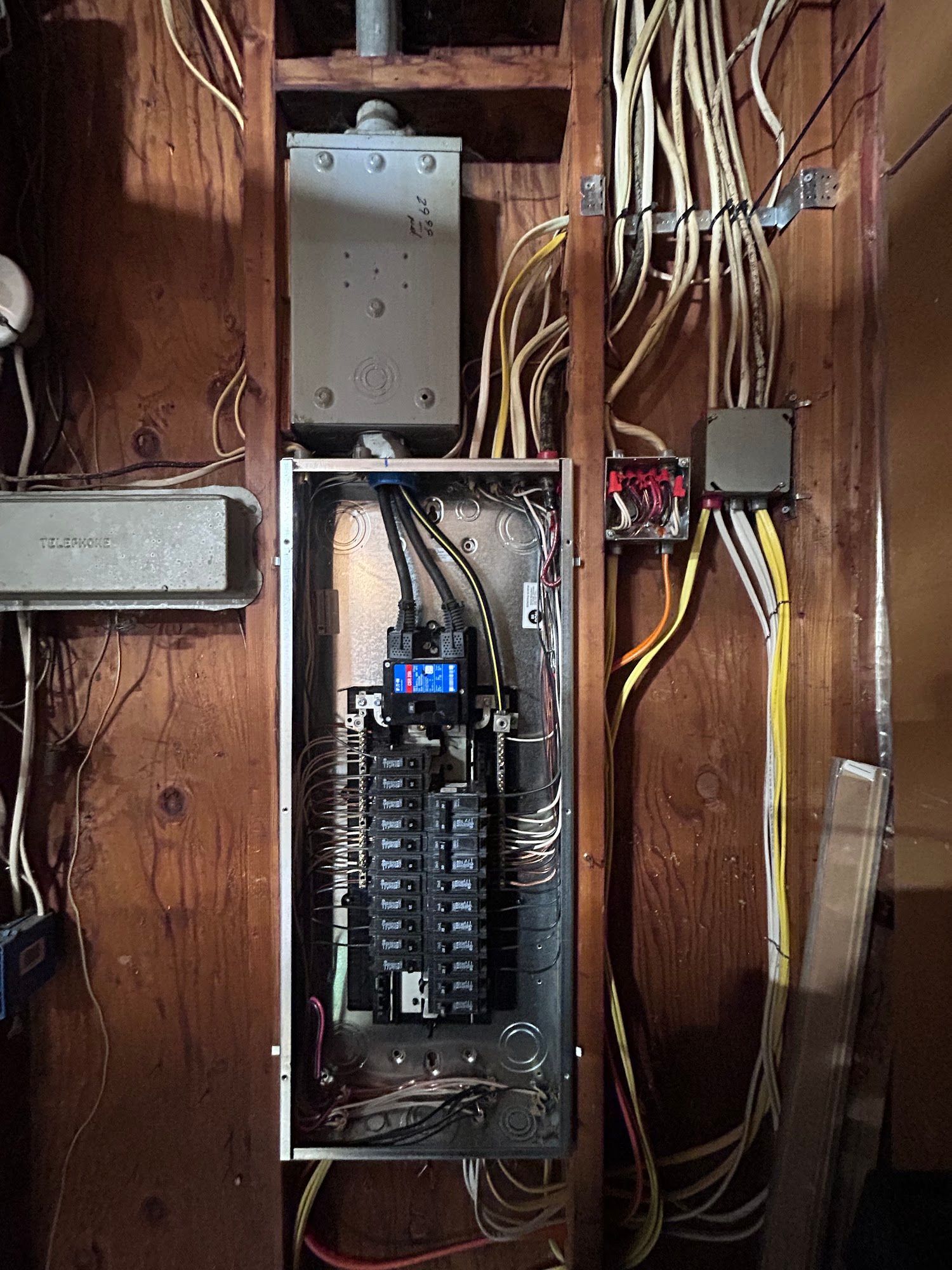 Electrical panel with numerous wires against a wood wall.