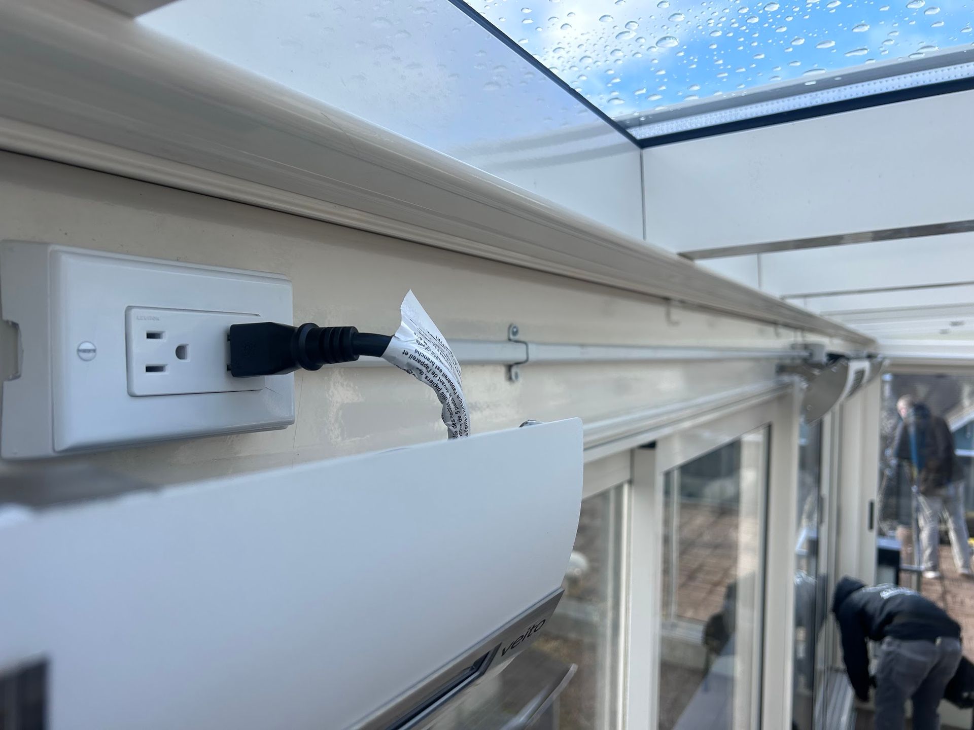 White electrical outlet with a plugged-in black cord, mounted on a wall near a window.
