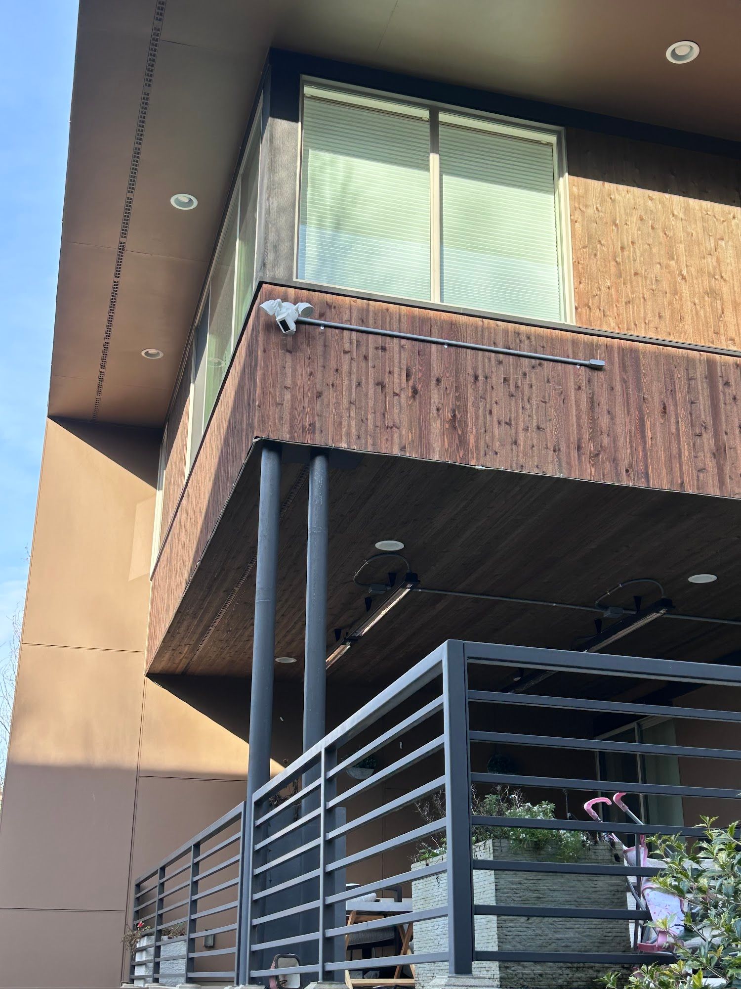 Modern building exterior with brown wood paneling, balcony, and black railings.