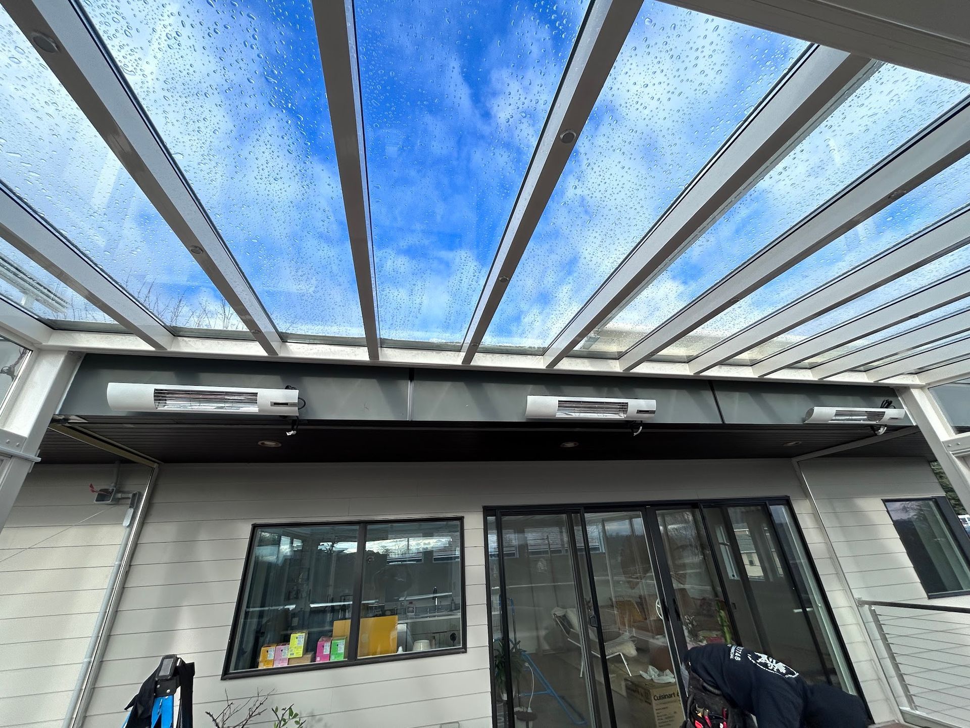 Clear-roofed outdoor area with heaters, overlooking a bright blue sky.