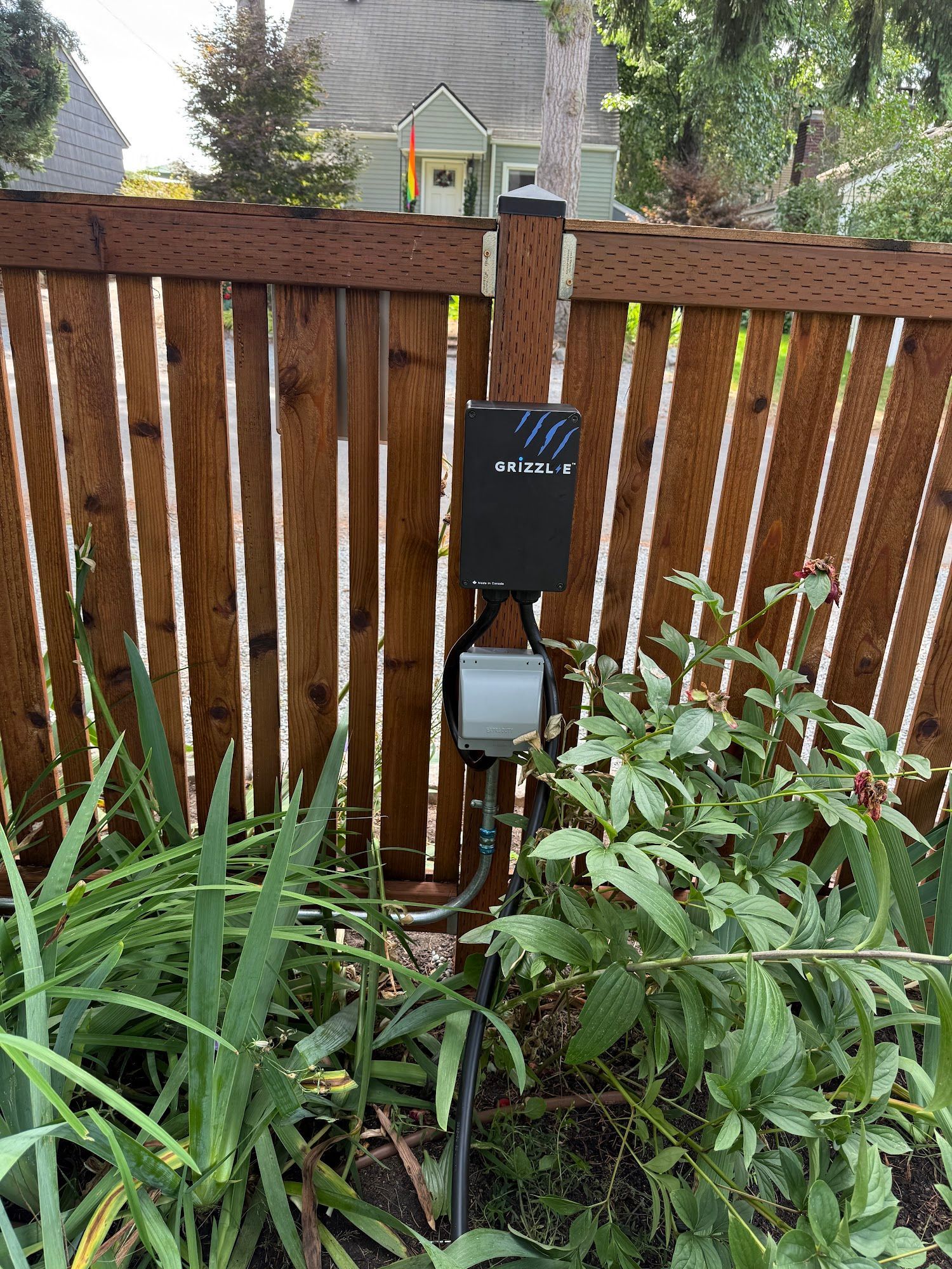 Black device mounted on a brown wooden fence, garden in front.