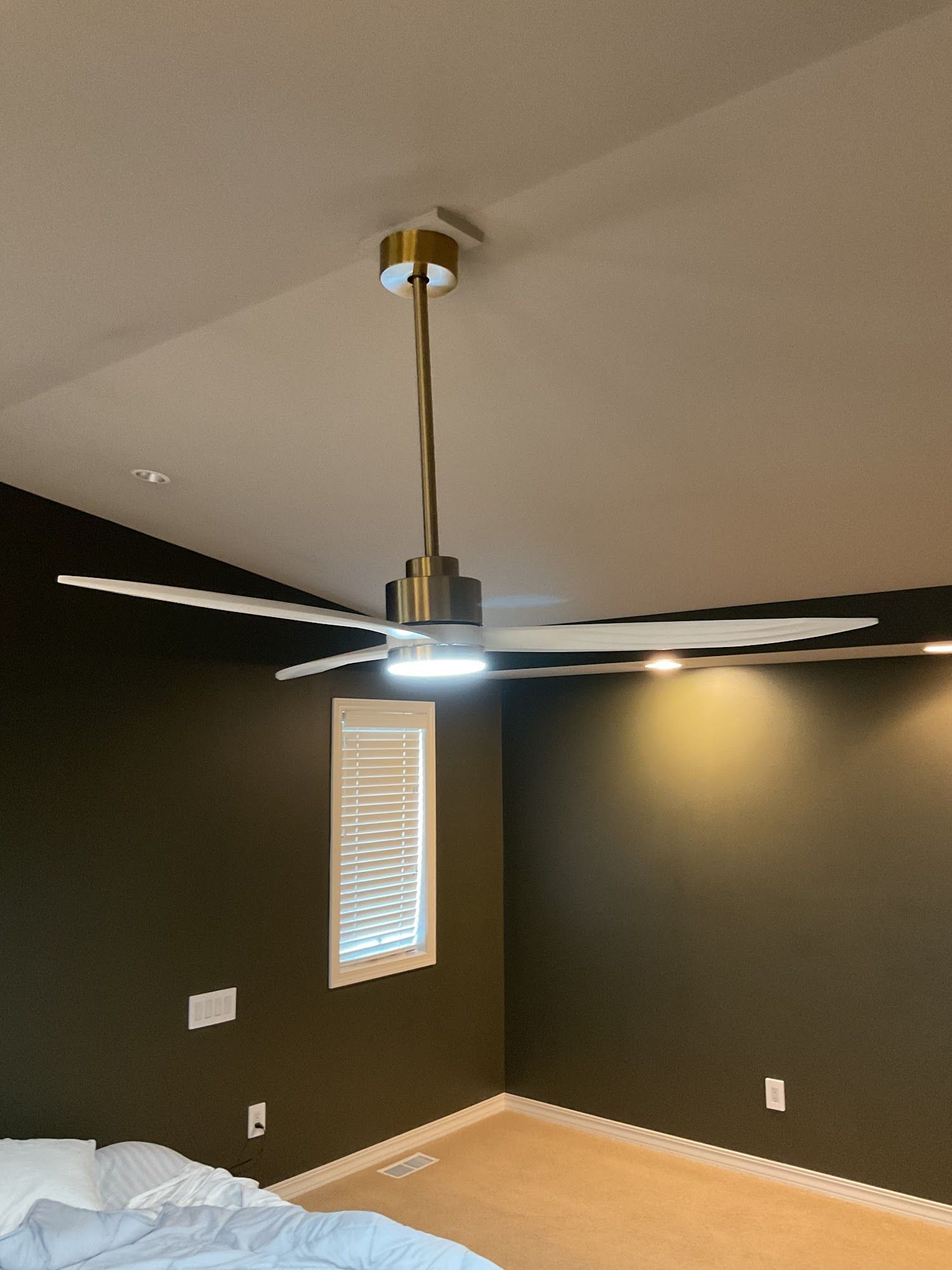 Ceiling fan with gold accents in a bedroom with dark green walls, a window with blinds, and a bed.