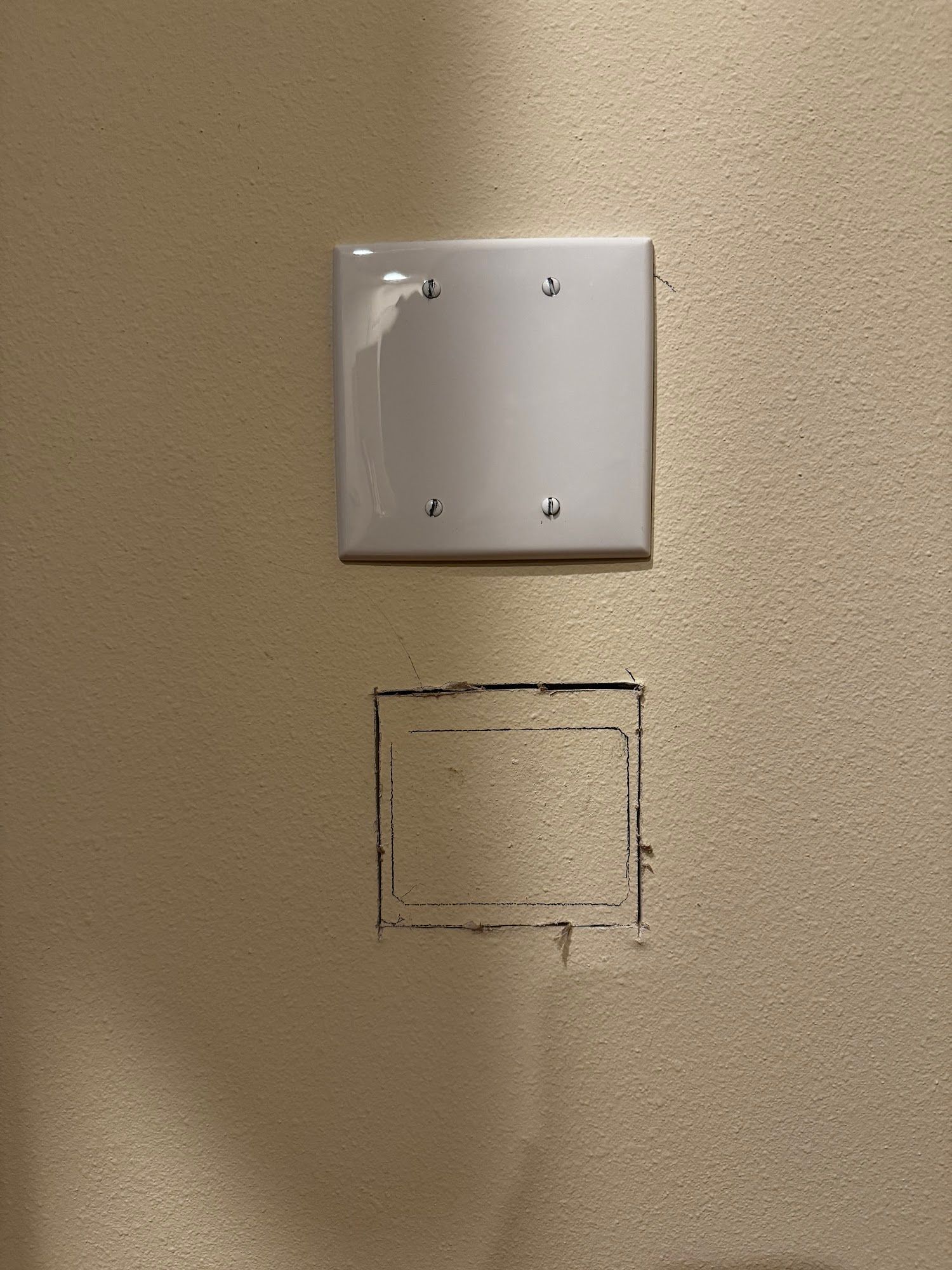 White electrical cover plate above a square hole in a beige wall.