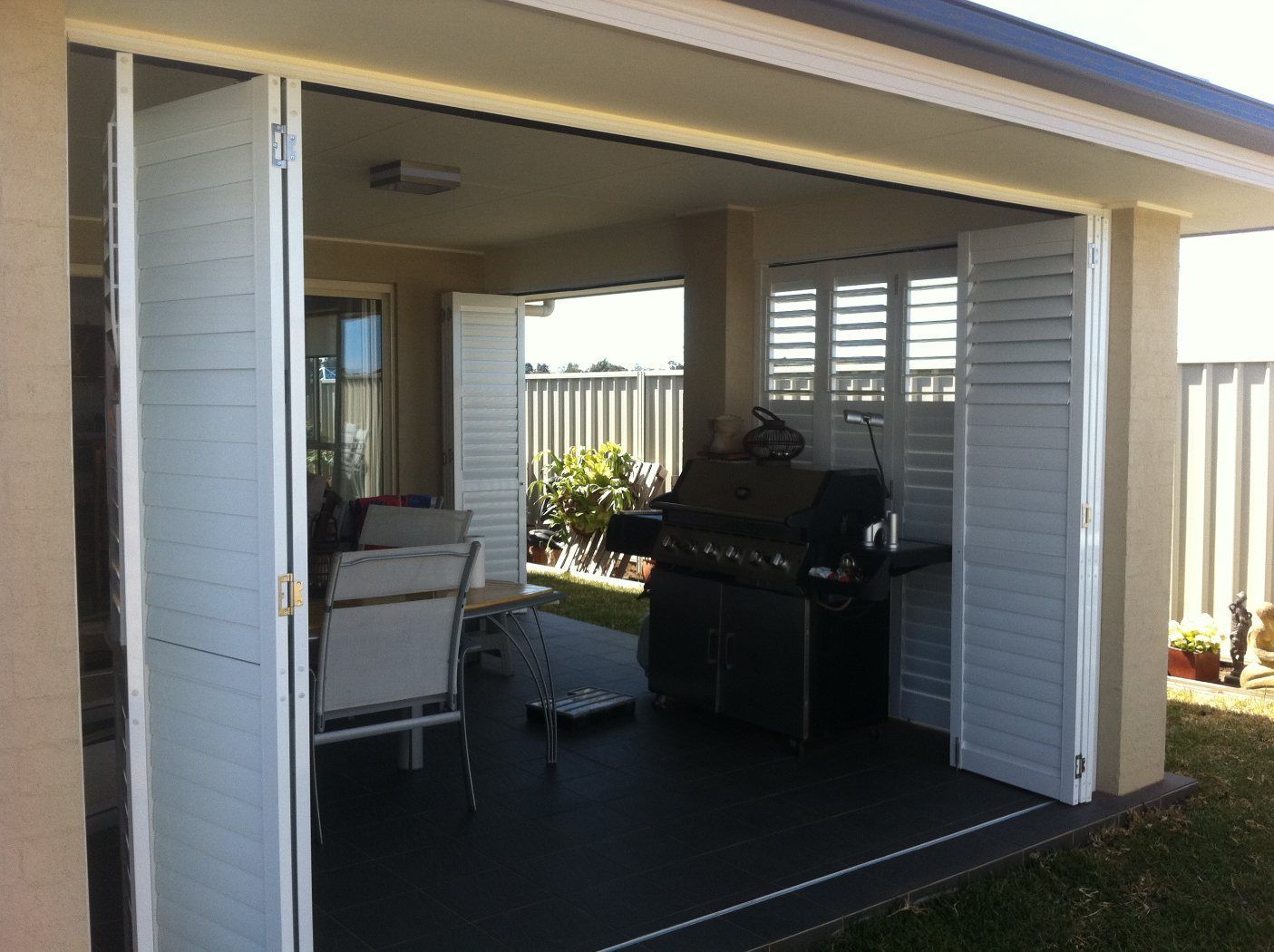 A Patio with A Grill and Chairs Behind a Sliding Glass Door — Lifestyle Aluminium Fabrication In Albion Park Rail, NSW
