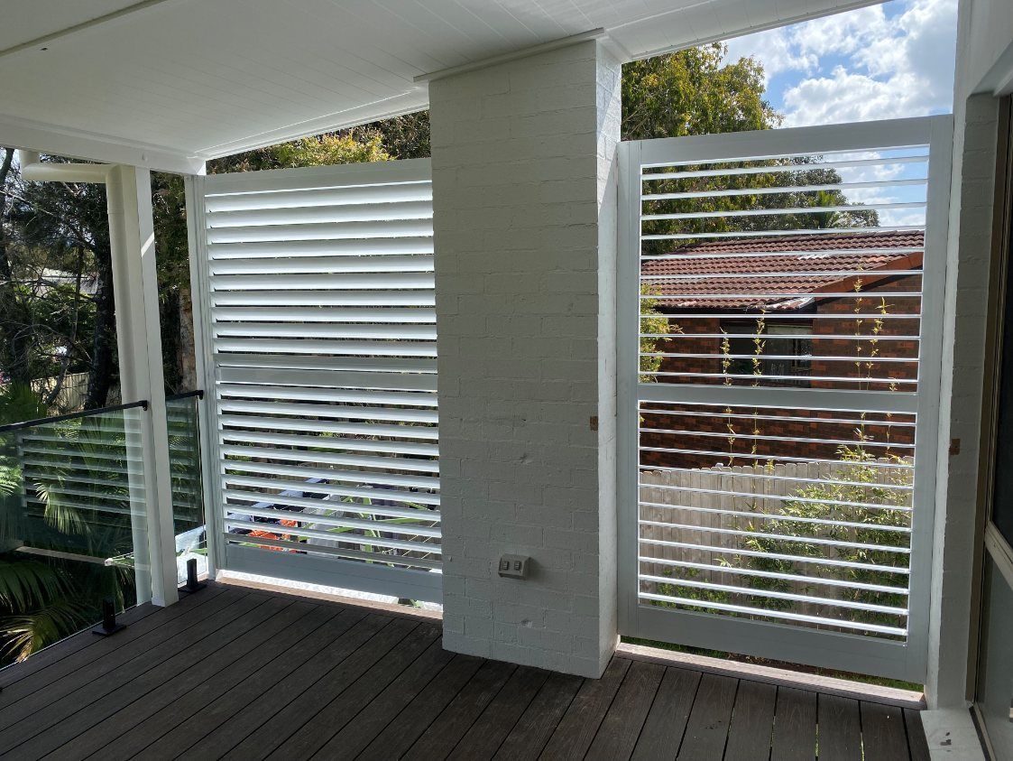 A White Shutter Is on The Side of A Building Next to A Wooden Deck — Lifestyle Aluminium Fabrication In Albion Park Rail, NSW