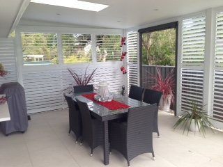 A Dining Room with A Table and Chairs and Shutters on The Windows — Lifestyle Aluminium Fabrication In Albion Park Rail, NSW