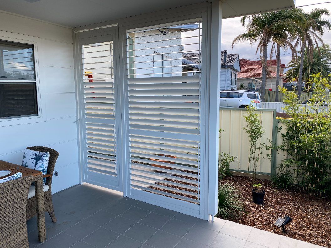 A Patio with A Table and Chairs and Shutters on The Windows — Lifestyle Aluminium Fabrication In Albion Park Rail, NSW