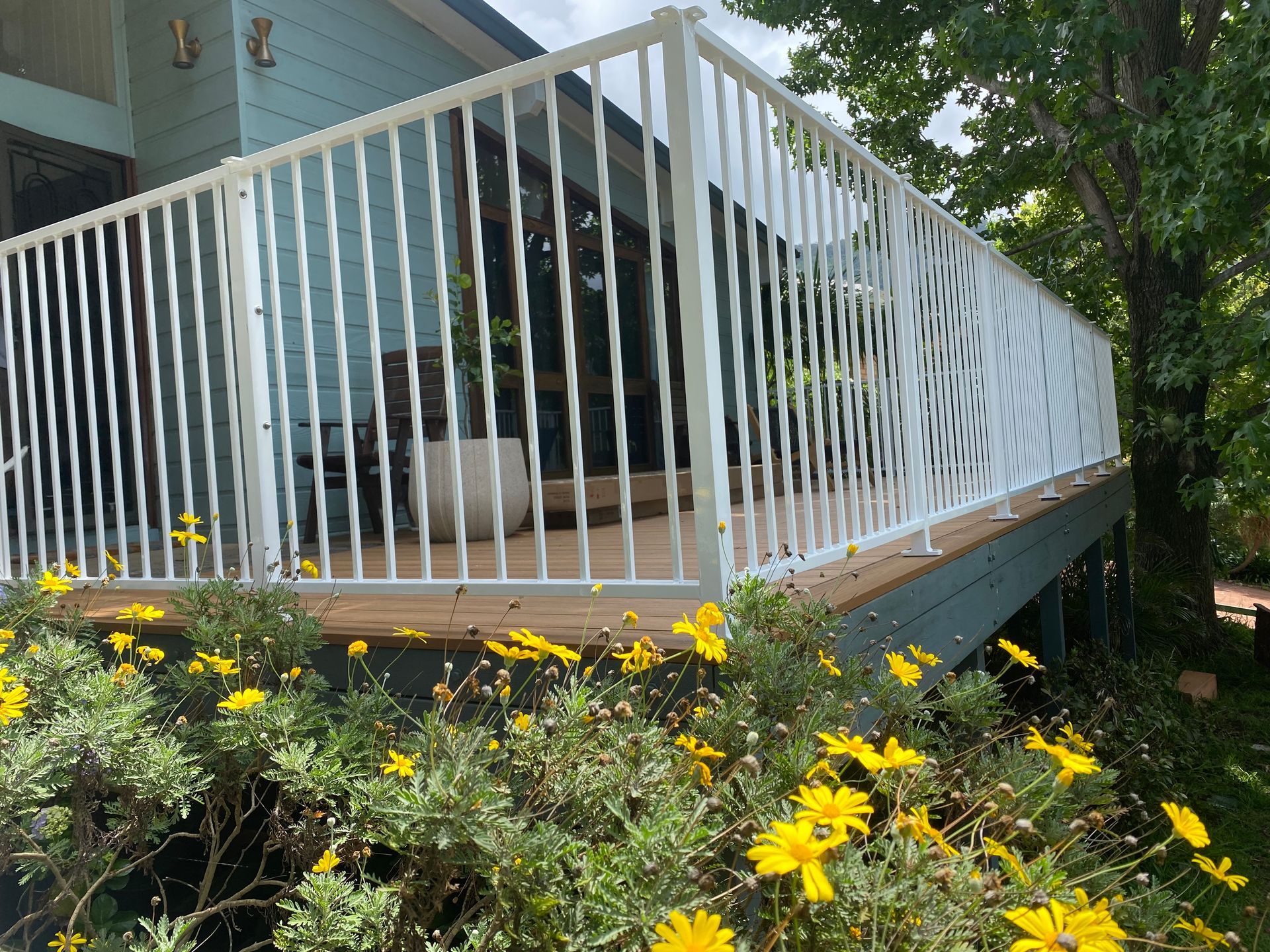 A deck with a white railing and yellow flowers in front of a house.