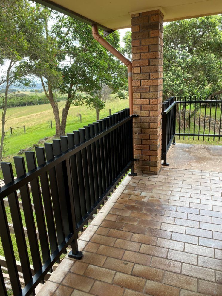A Balcony with A Black Railing and A Brick Column — Lifestyle Aluminium Fabrication In Albion Park Rail, NSW