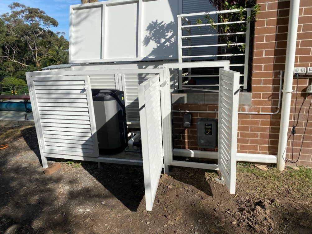 A White Fence Is Sitting in Front of A Brick Building — Lifestyle Aluminium Fabrication In Albion Park Rail, NSW