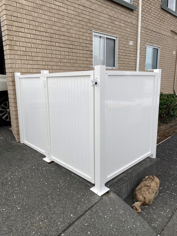 A White Fence Is Sitting in Front of A Brick Building — Lifestyle Aluminium Fabrication In Albion Park Rail, NSW
