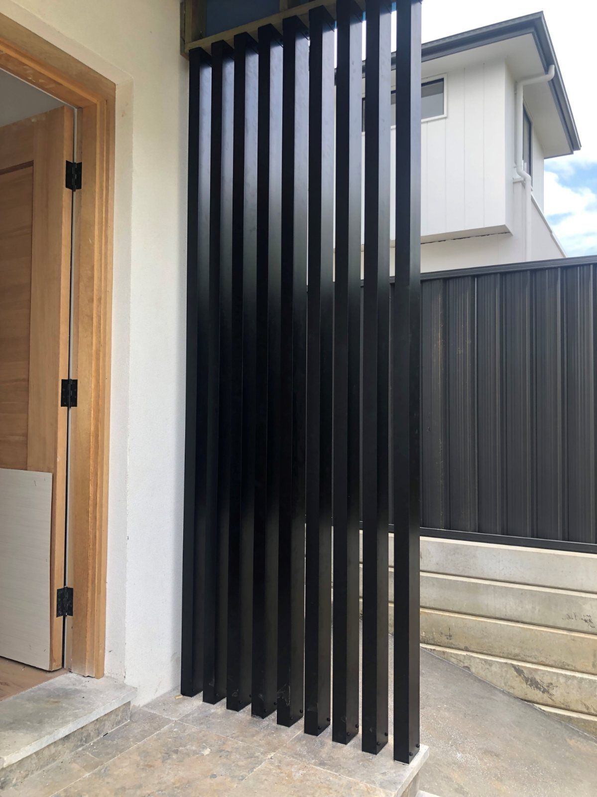 A Black Fence Is Sitting Next to A Door in Front of A House — Lifestyle Aluminium Fabrication In Albion Park Rail, NSW