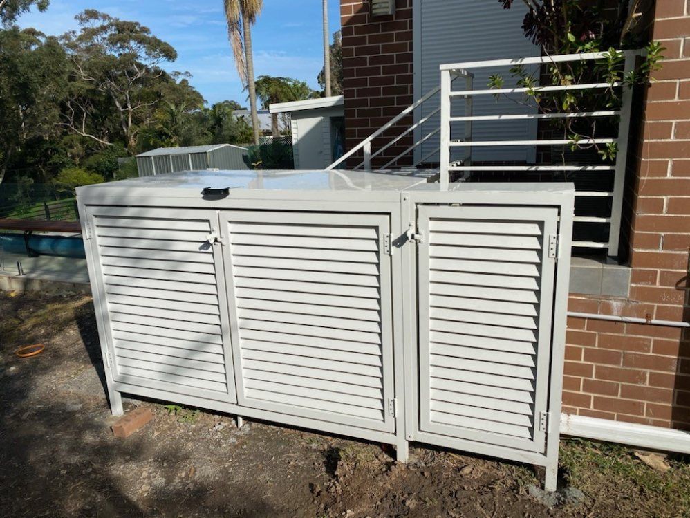 A White Fence Is Surrounding a Brick Building — Lifestyle Aluminium Fabrication In Albion Park Rail, NSW