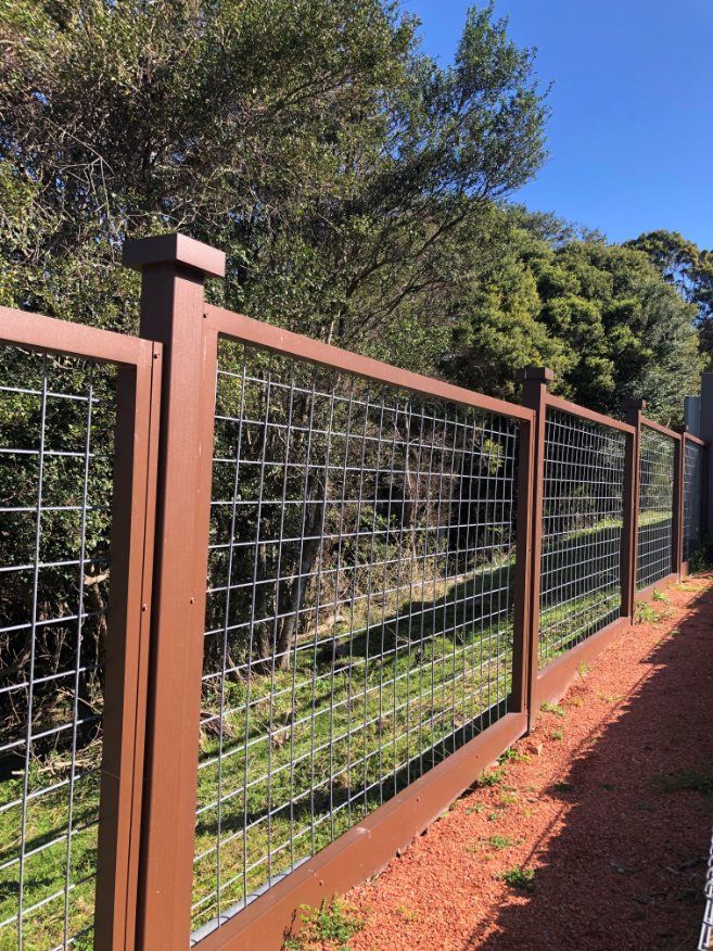 A Brown Fence with A Wire Mesh Is Surrounded by Trees — Lifestyle Aluminium Fabrication In Albion Park Rail, NSW