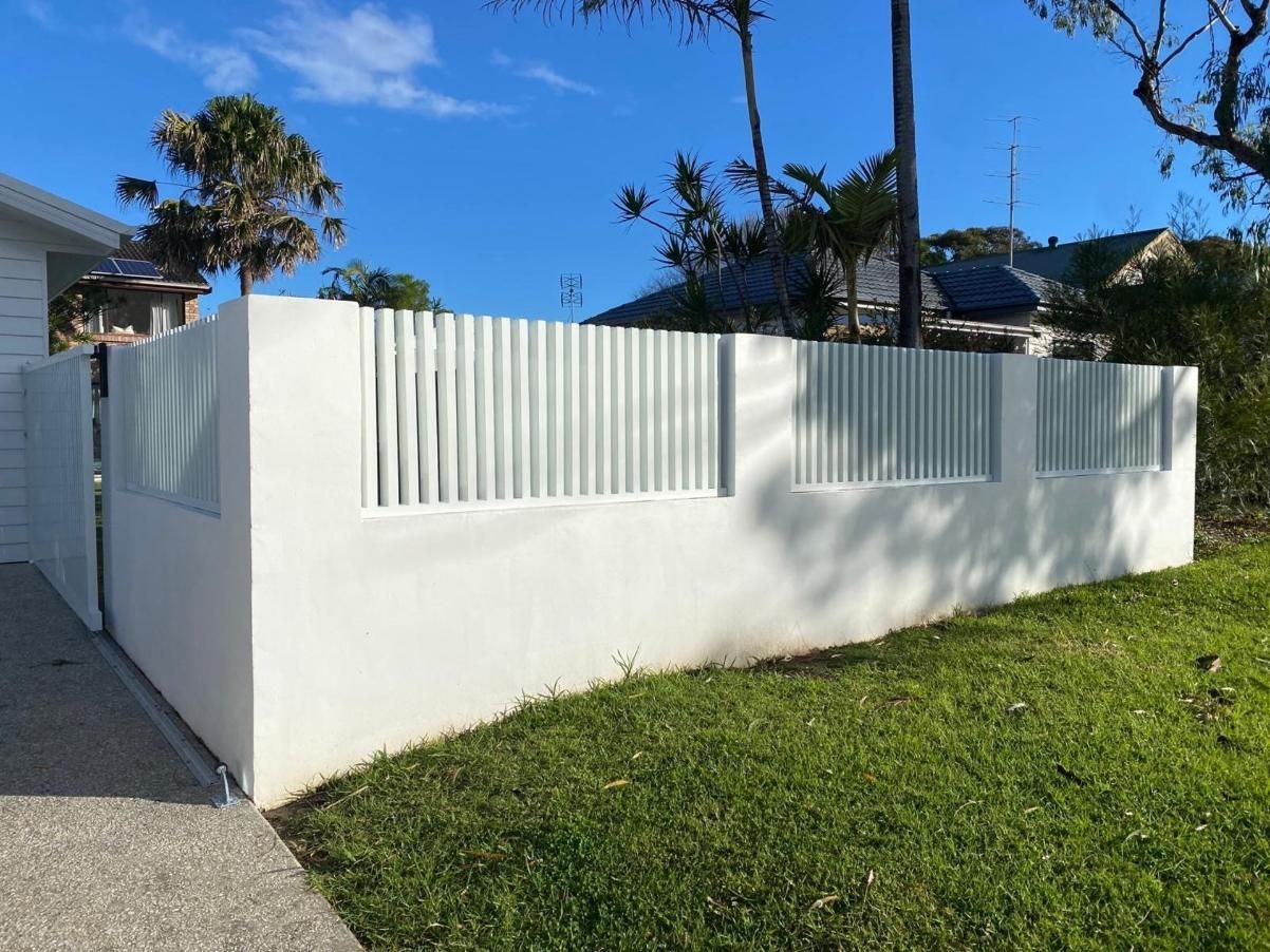 A White Fence Is Surrounded By Grass And Trees In Front Of A House — Lifestyle Aluminium Fabrication In Albion Park Rail, NSW