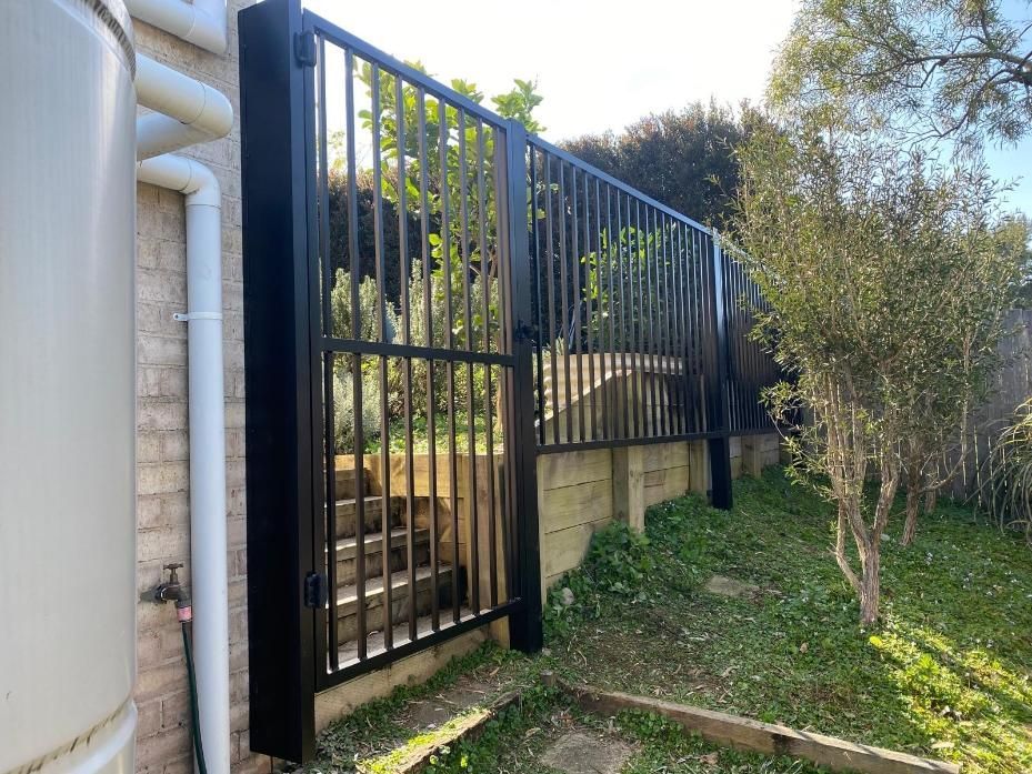 A Black Gate is Sitting Next to a Brick Wall — Lifestyle Aluminium Fabrication In Kiama, NSW