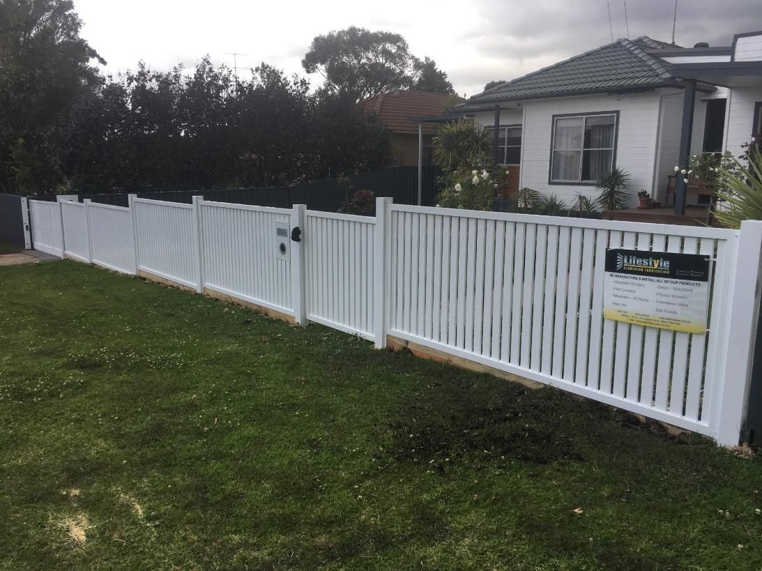 A White Fence Surrounds a Lush Green Yard in Front of a House — Lifestyle Aluminium Fabrication In Shellharbour, NSW